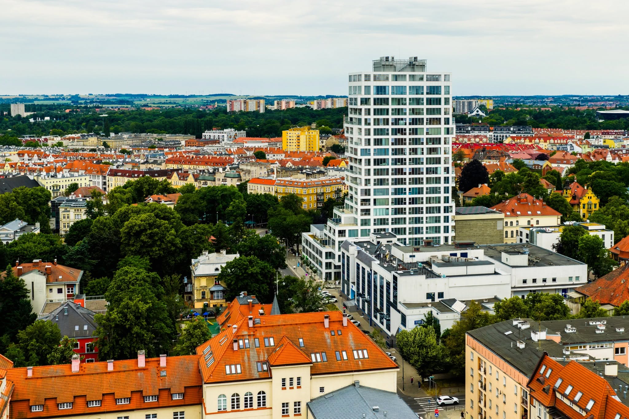 Panorama miasta z białym wieżowcem i czerwonymi dachami kamienic.