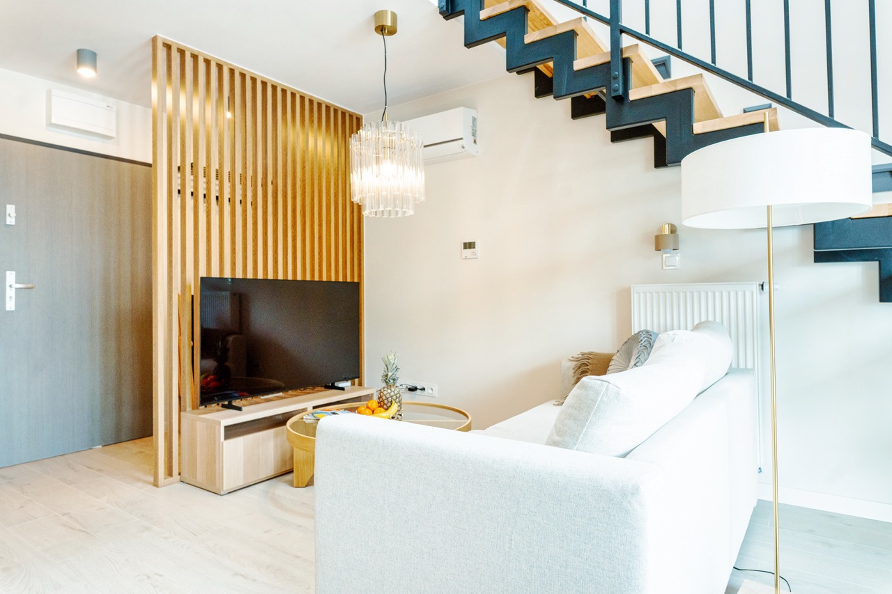 Salon z sofą, telewizorem i schodami na antresolę w apartamencie