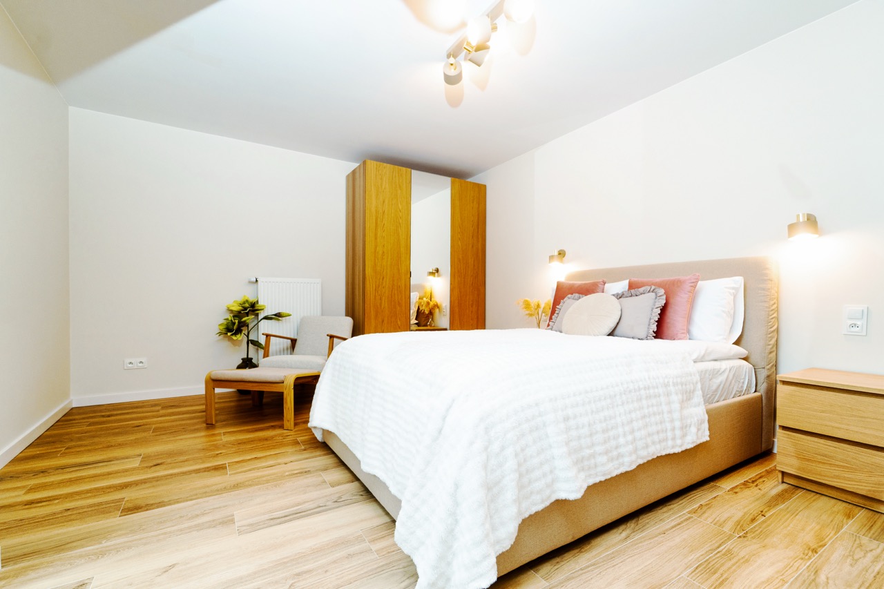 Jasna sypialnia z dużym łóżkiem, szafą i fotelem w apartamencie