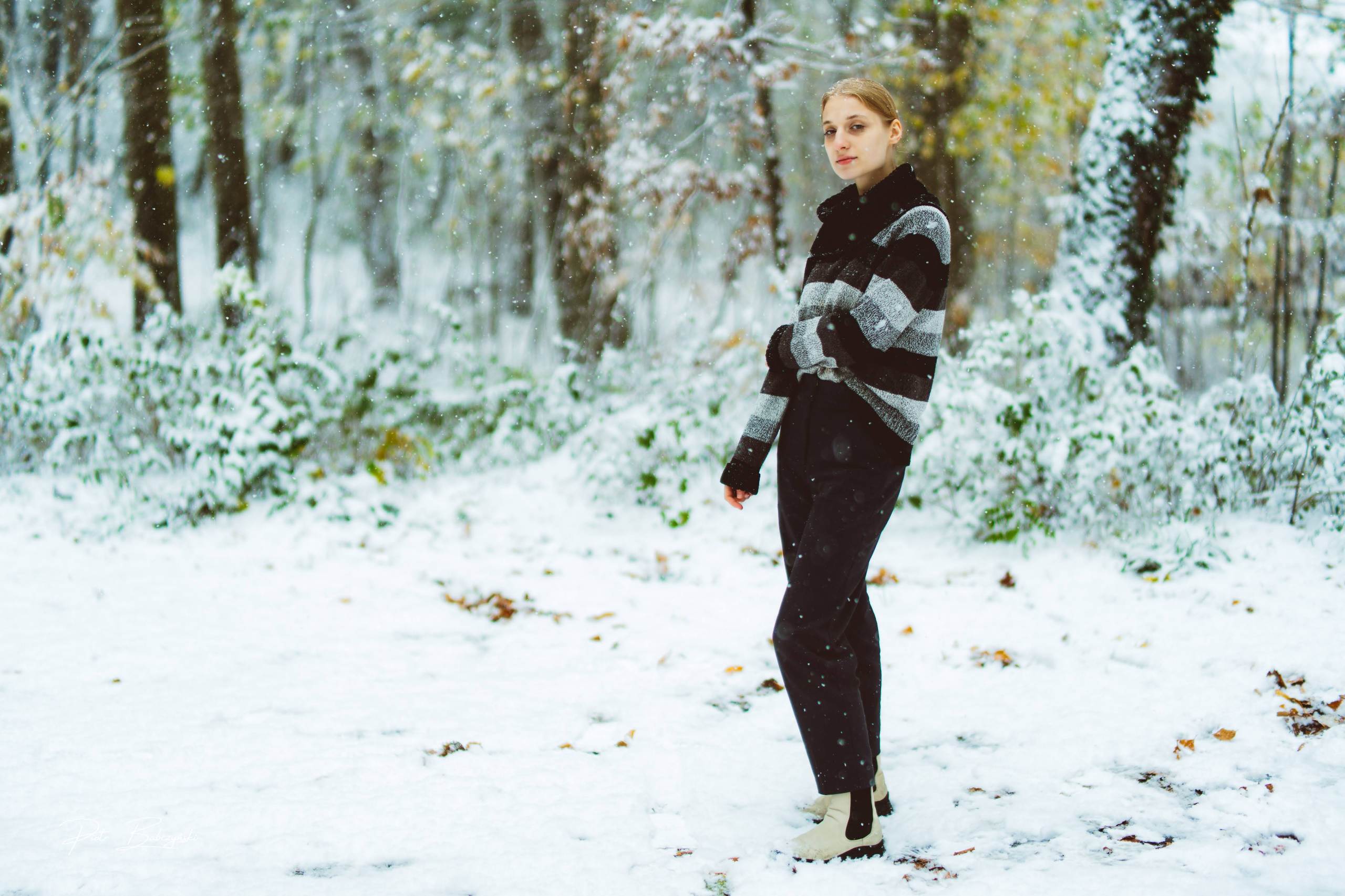 Fotografia modowa w zimowej scenerii — modelka w stylowym swetrze i czarnych spodniach na tle zaśnieżonego lasu w Szczecinie.