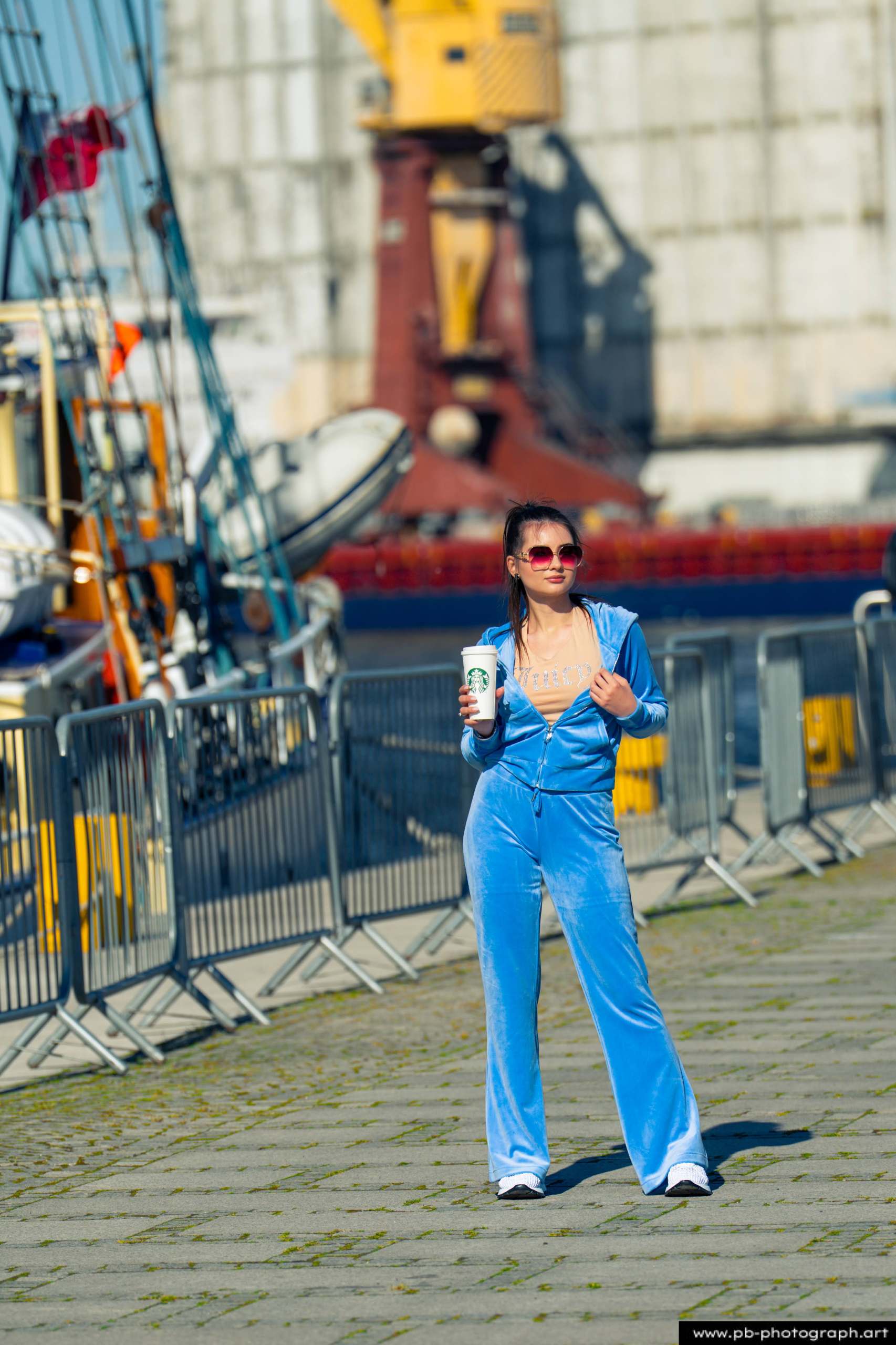 Fotografia produktowa na Łasztowni w Szczecinie — modelka w niebieskim dresie z napojem w dłoni.
