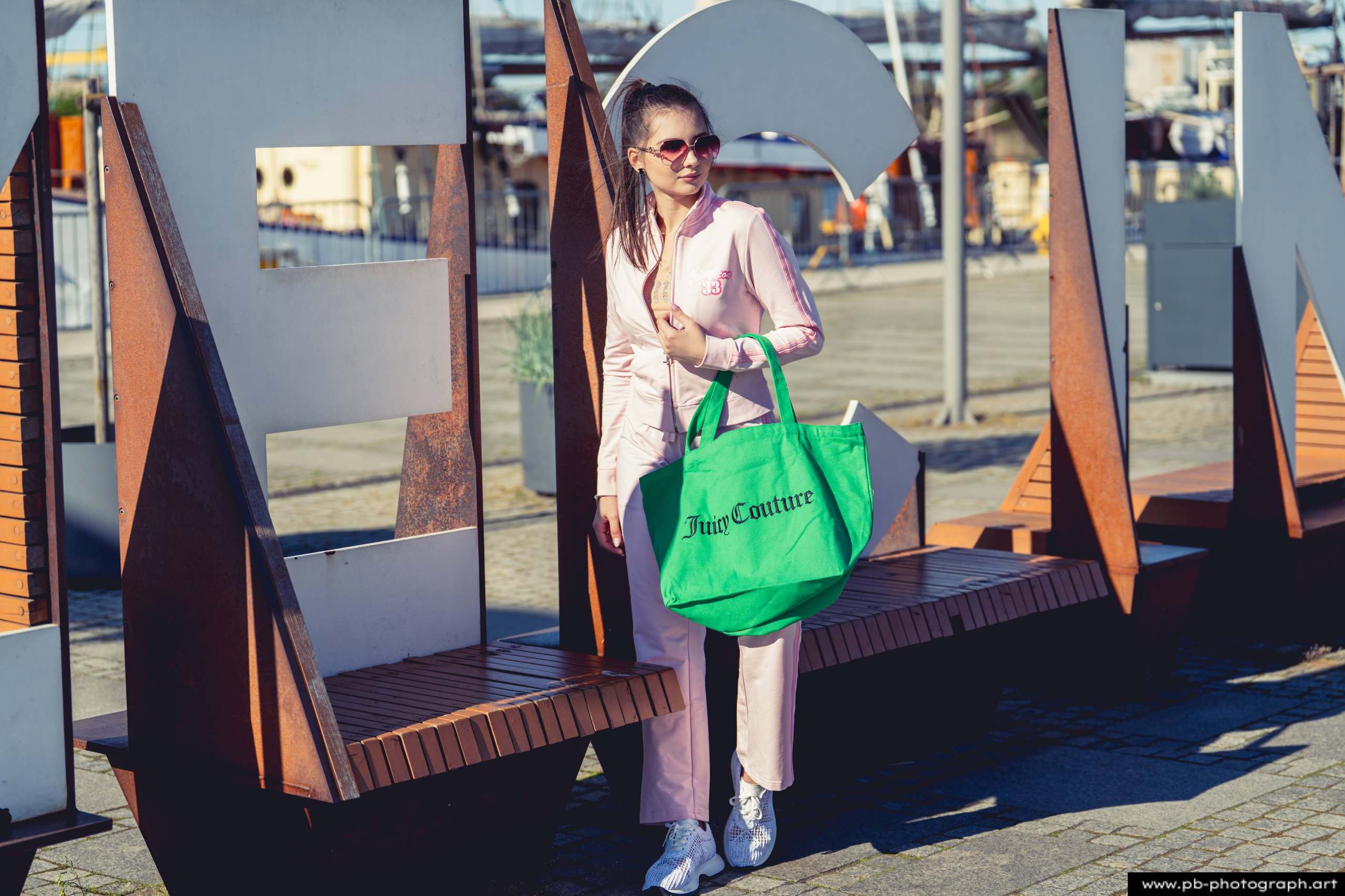 Fotografia produktowa na Łasztowni w Szczecinie — modelka w różowym dresie z zieloną torbą marki odzieżowej.