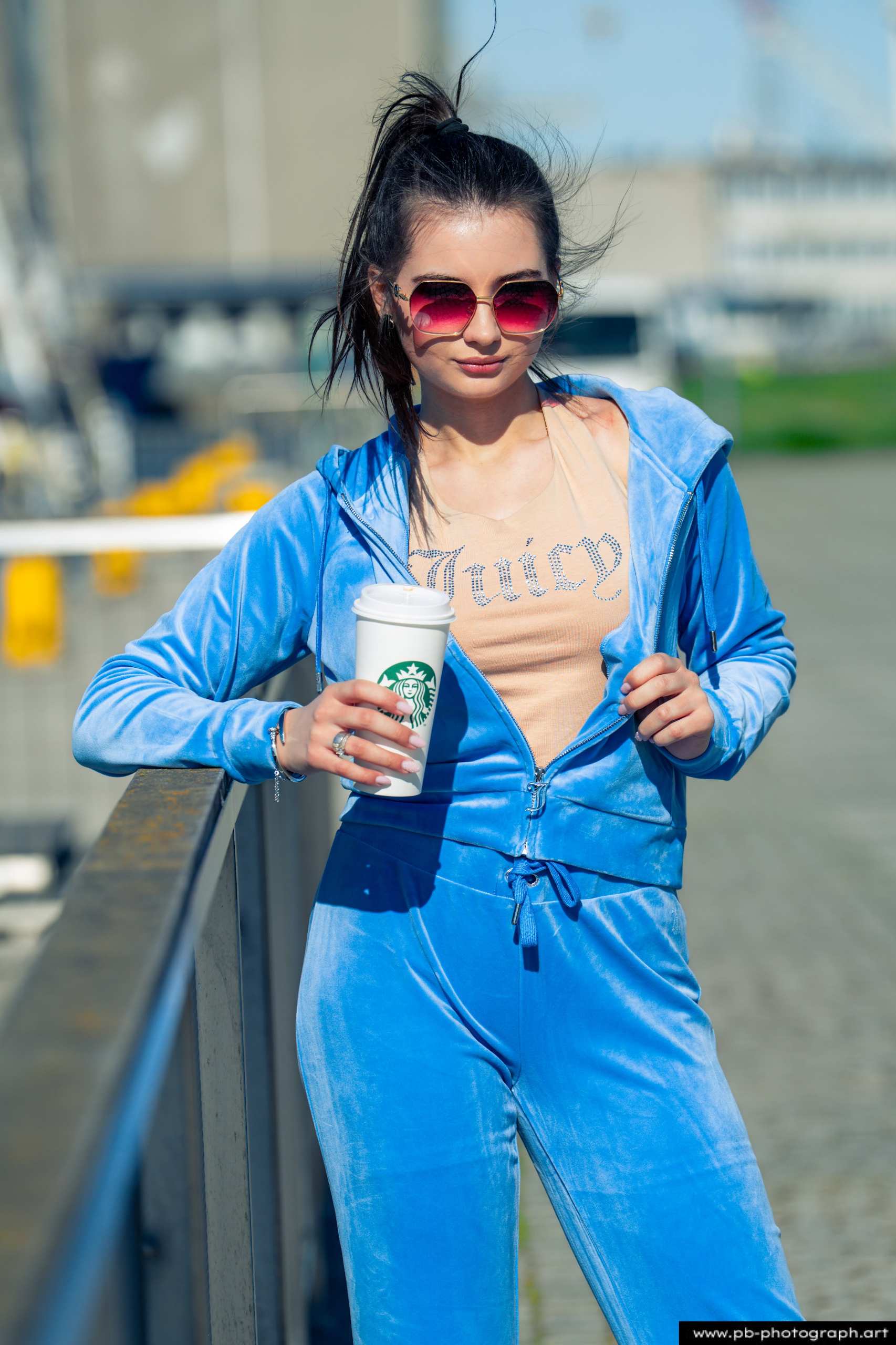 Fotografia produktowa na Łasztowni w Szczecinie — modelka w niebieskim dresie z napisem, trzymająca kawę.