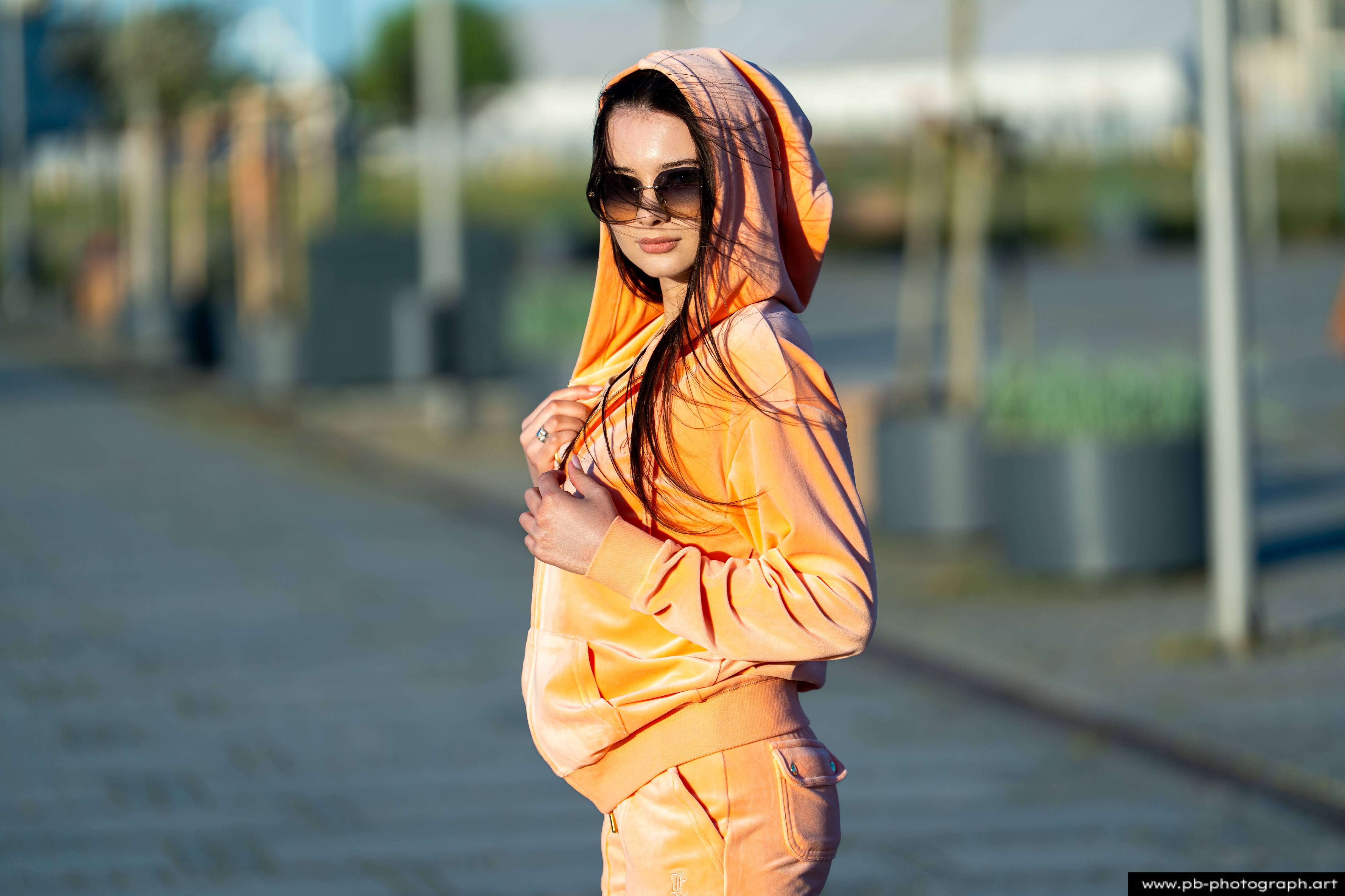 Fotografia produktowa na Łasztowni w Szczecinie — modelka w pomarańczowym dresie z kapturem.