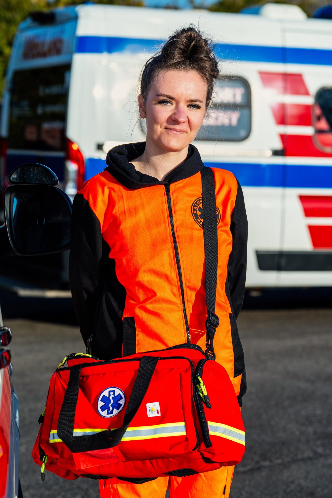 Portret pracownika transportu medycznego w Szczecinie, w pomarańczowym uniformie z torbą medyczną.