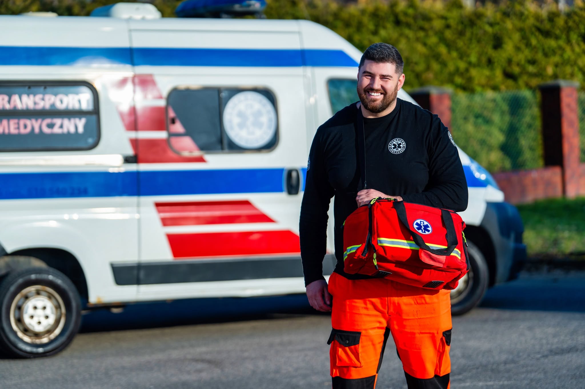 Fotografia wizerunkowa — pracownik transportu medycznego RMED z torbą ratunkową przed pojazdem w Szczecinie.