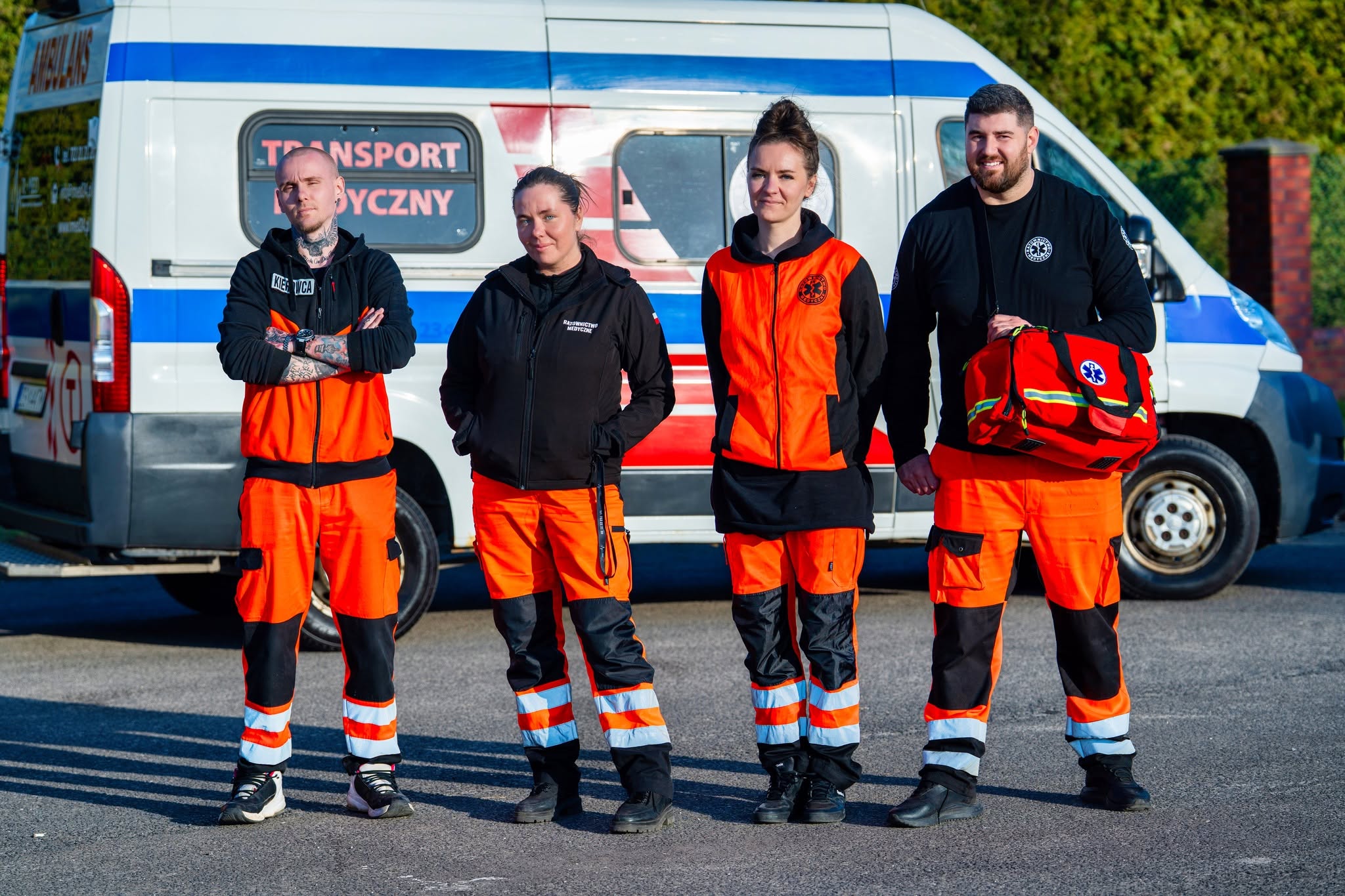 Zespół pracowników RMED w pomarańczowych uniformach medycznych przed karetką w Szczecinie.