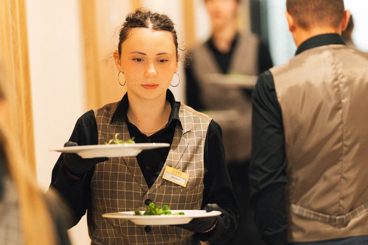 Fotografia eventowa z kolacji degustacyjnej w Szczecinie — kelnerka serwująca dania gościom.