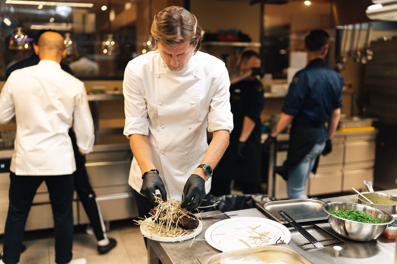 Fotografia eventowa z kolacji degustacyjnej w Szczecinie — Karol Okrasa przygotowuje danie w luksusowej restauracji.
