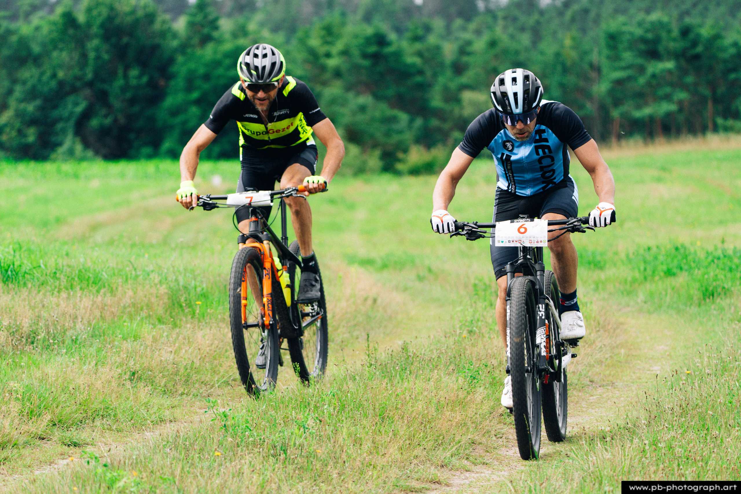 Ujęcie z drona dwóch zawodników MTB na trasie wyścigu w Szczecinie, z widokiem na zieloną okolicę.
