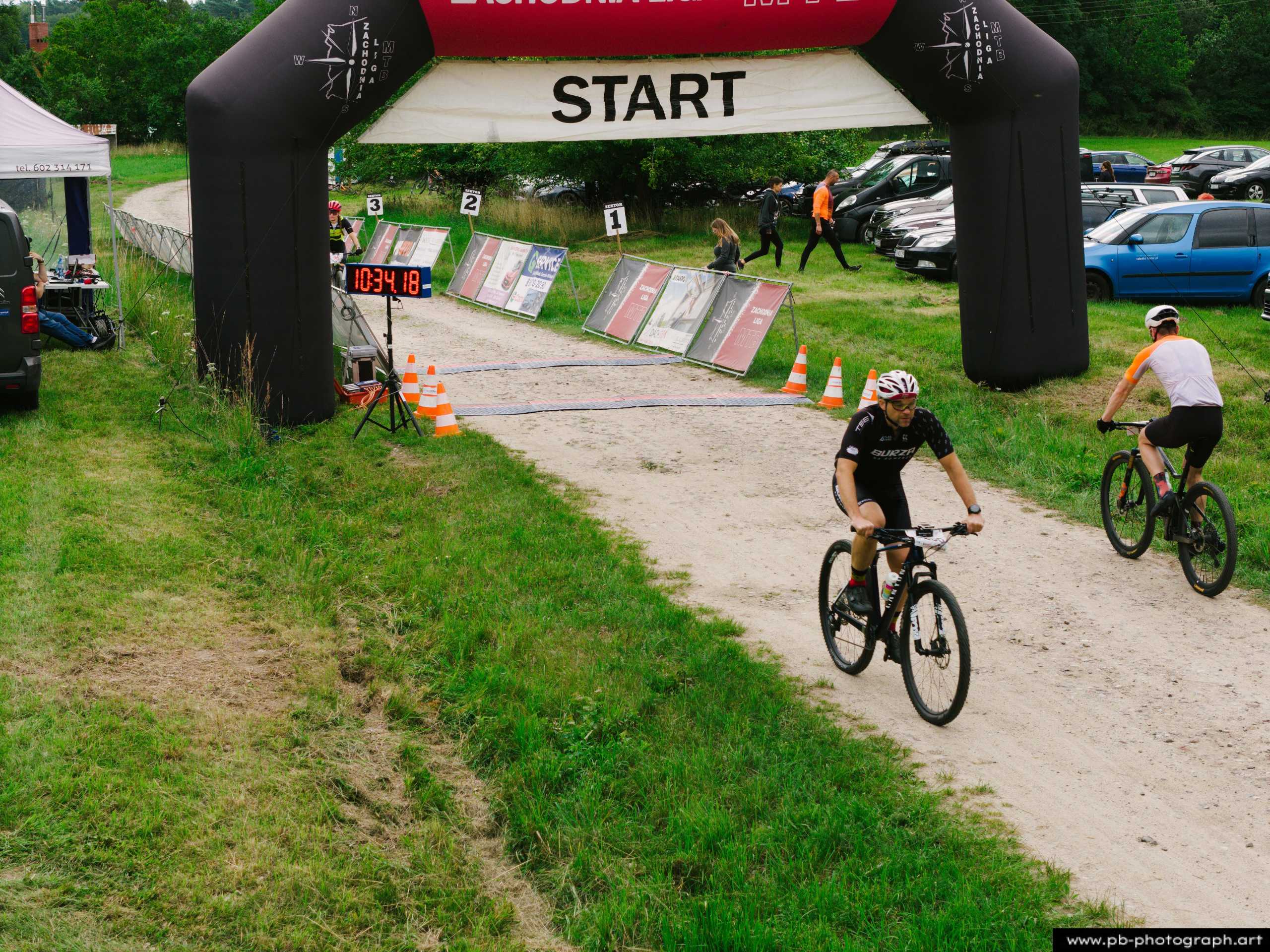 Ujęcie z drona na trasie wyścigu MTB w Szczecinie — zawodnicy zbliżają się do mety pod balonem startowym.
