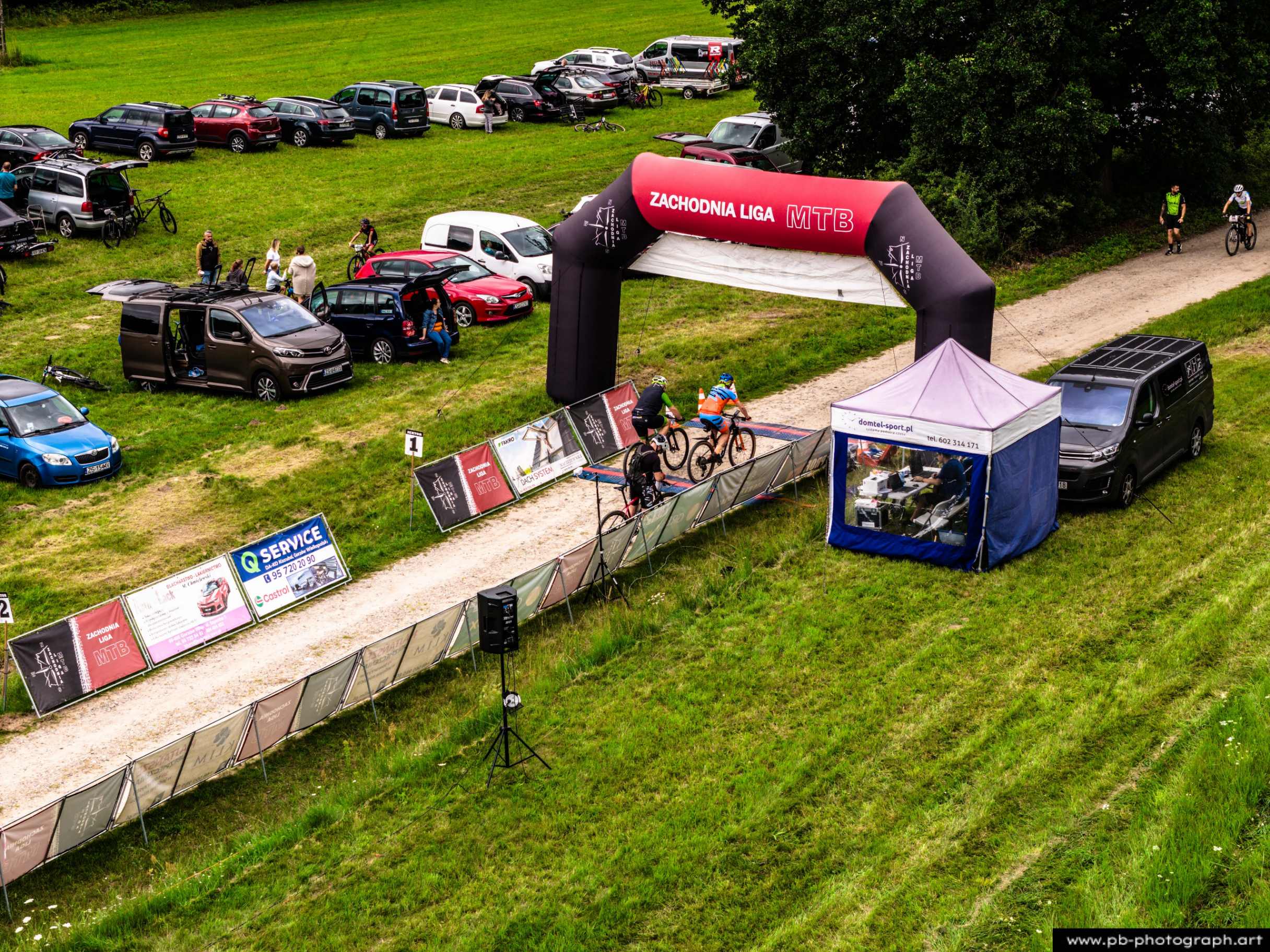 Ujęcie z drona na trasie wyścigu MTB w Szczecinie, z zawodnikami przejeżdżającymi przez bramę startową.