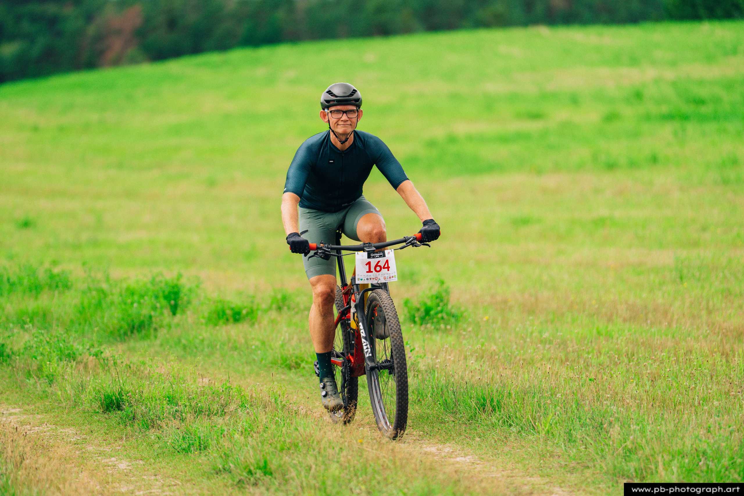 Zawodnik na rowerze górskim w trakcie wyścigu MTB na zielonym tle w Szczecinie.