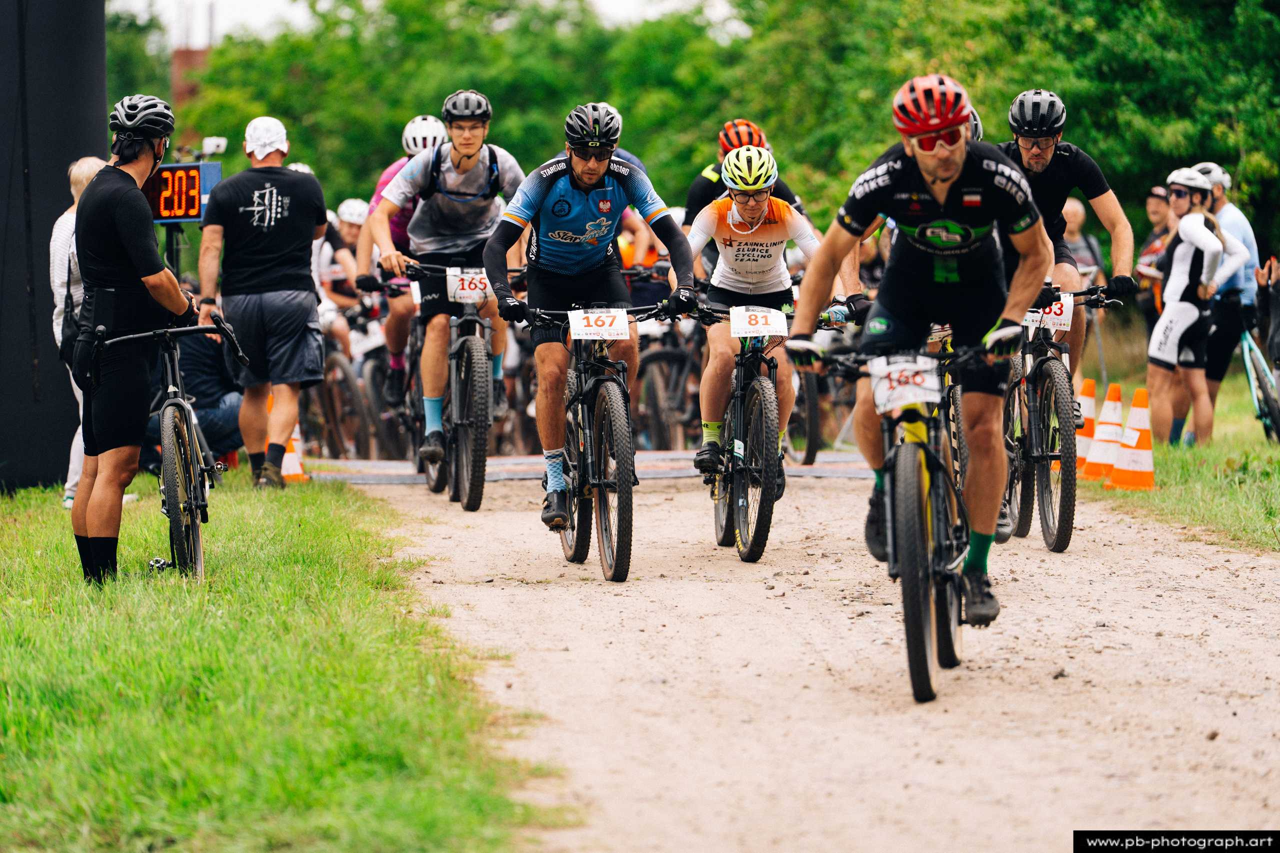 Ujęcie z drona na zawodników MTB startujących na trasie wyścigu w Szczecinie, z widocznymi numerami na koszulkach.
