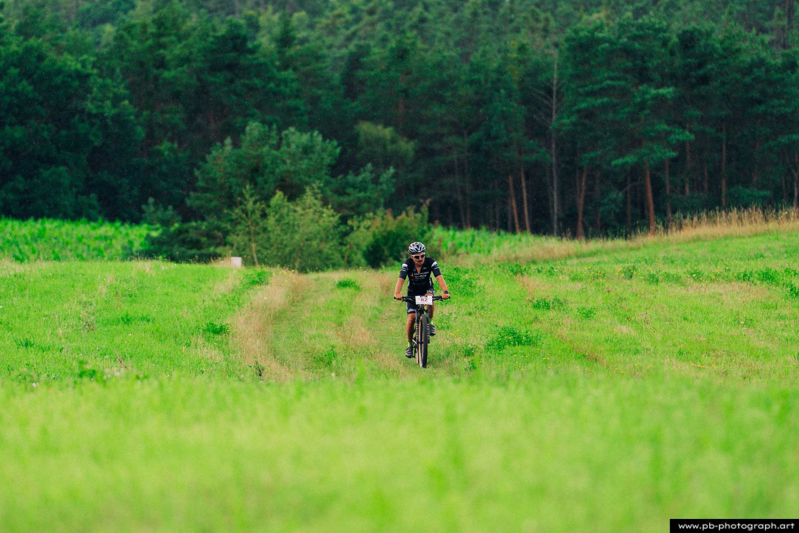 Ujęcie z drona zawodnika MTB na trasie wyścigu, otoczonego zielonymi polami w Szczecinie.