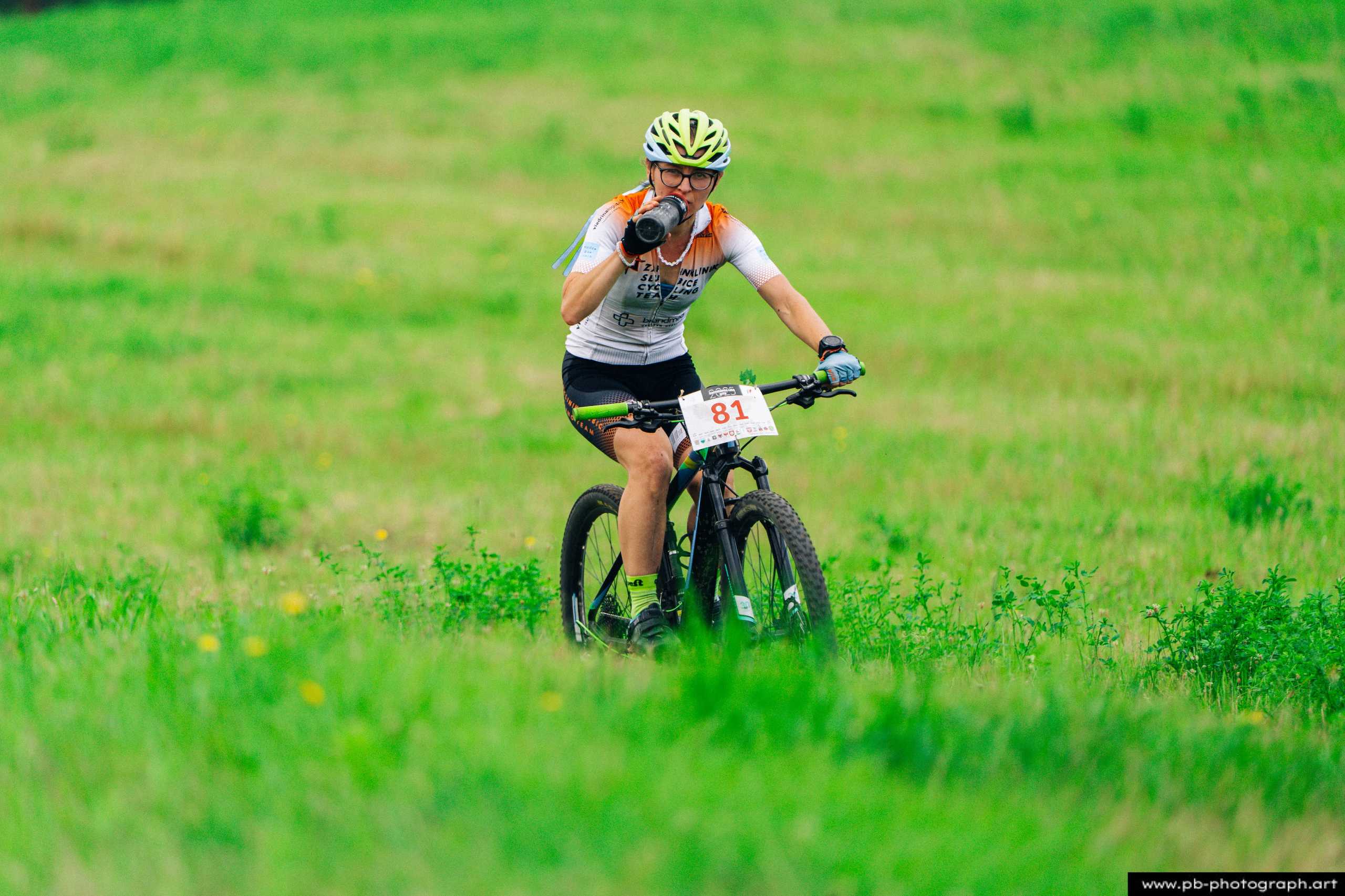 Zawodniczka na rowerze górskim podczas wyścigu MTB w Szczecinie, z widokiem na zieloną, trawiastą trasę.