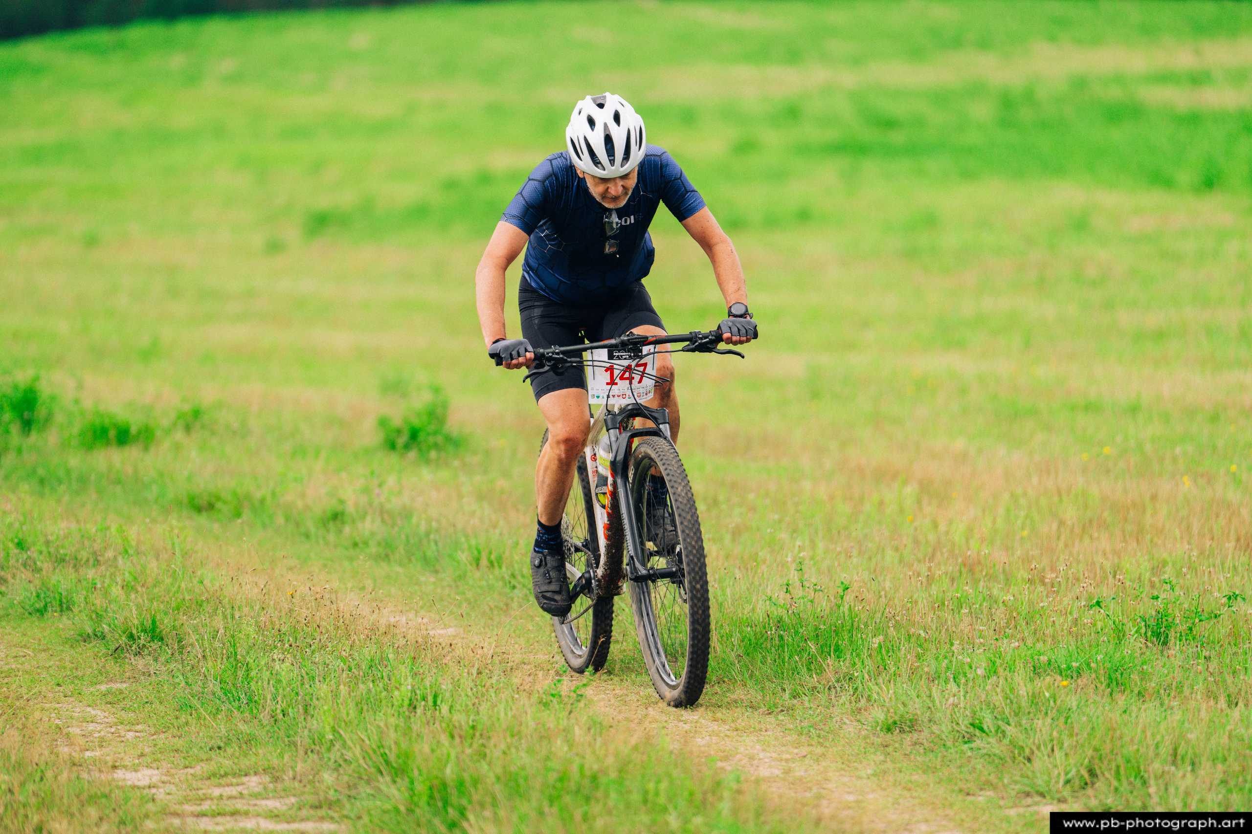 Zawodnik na rowerze górskim podczas wyścigu MTB w Szczecinie, pokonujący zieloną trasę w terenie.
