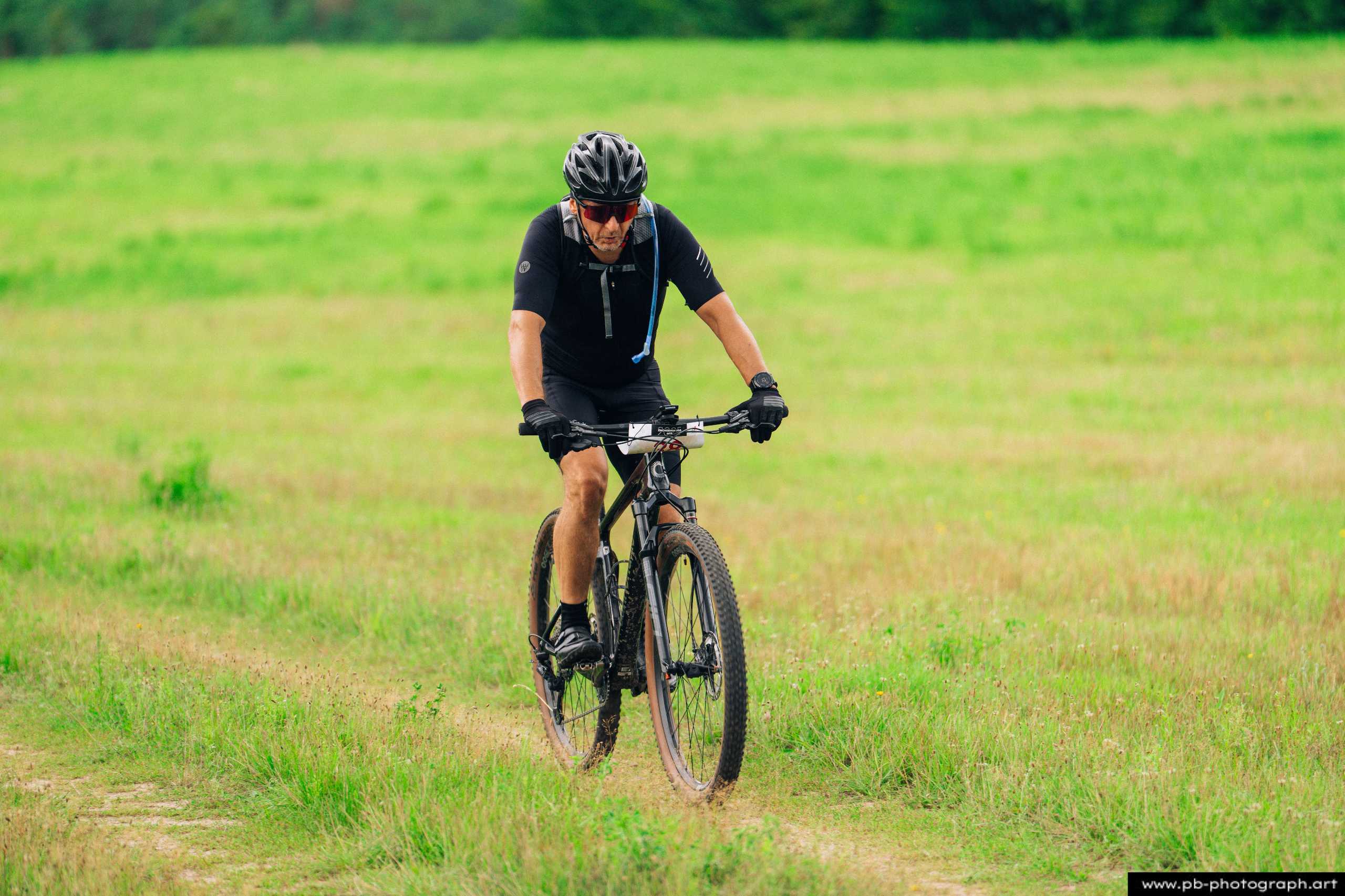 Ujęcie z drona zawodnika MTB na trasie wyścigu w Szczecinie, pokonującego zieloną, otwartą przestrzeń.
