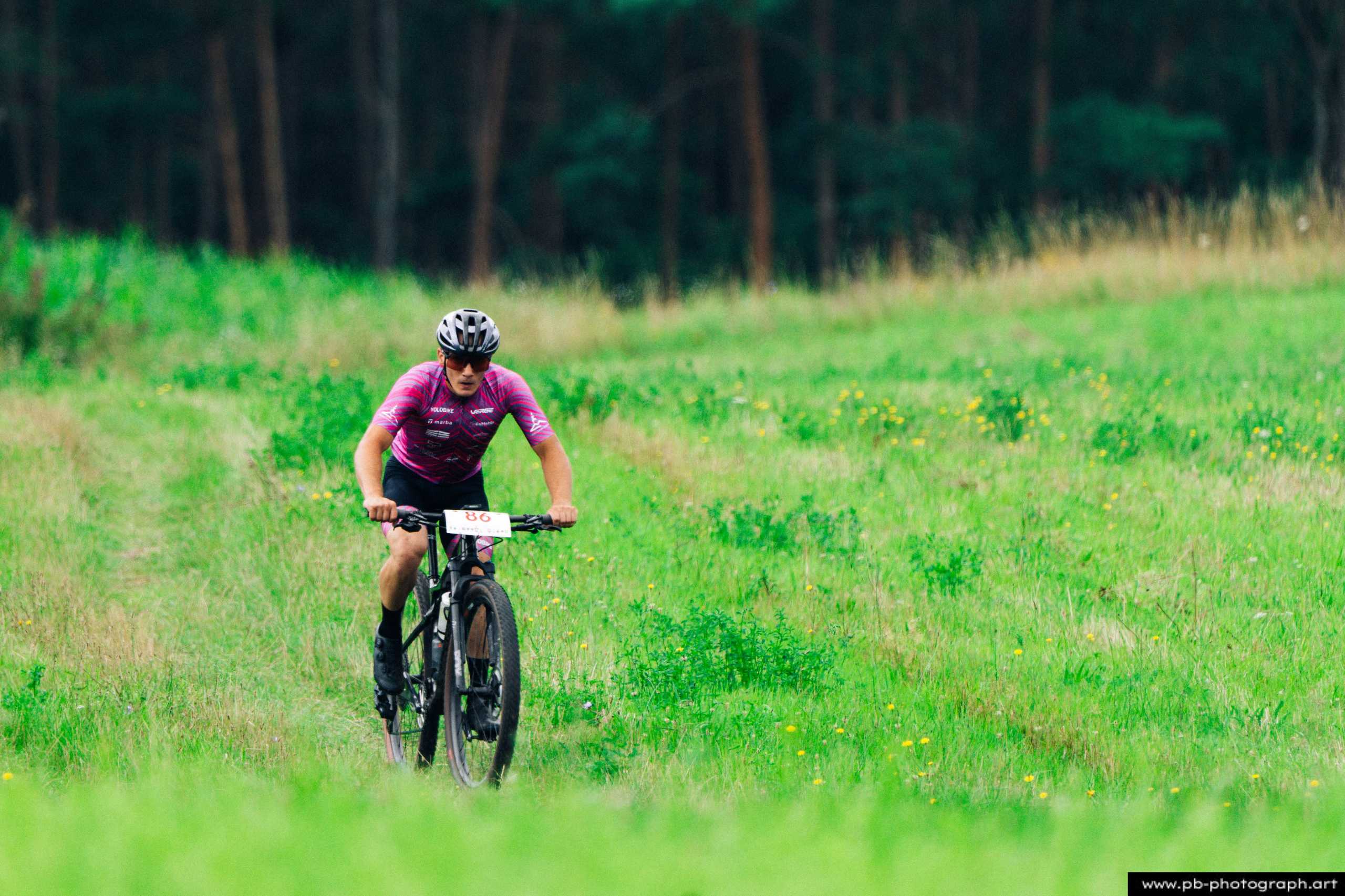 Fotografia z drona przedstawiająca zawodnika MTB na trasie w Szczecinie, w otoczeniu zielonych łąk i drzew.
