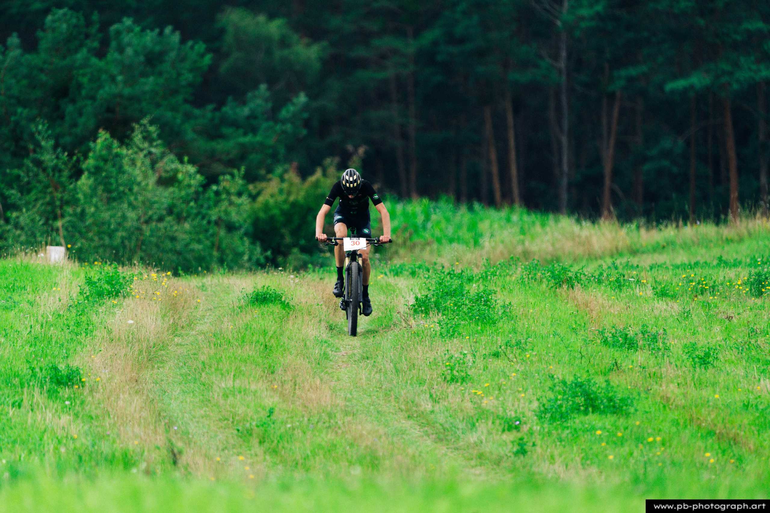 Ujęcie z drona zawodnika MTB na zielonej trasie wyścigu w Szczecinie, otoczonym lasem.