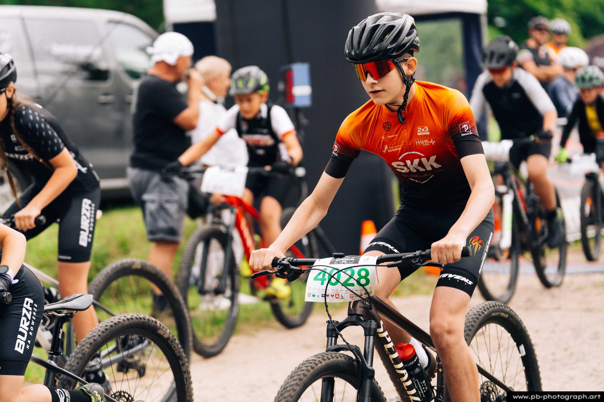 Młody zawodnik na rowerze górskim w pomarańczowej koszulce, przygotowujący się do startu w wyścigu MTB w Szczecinie.