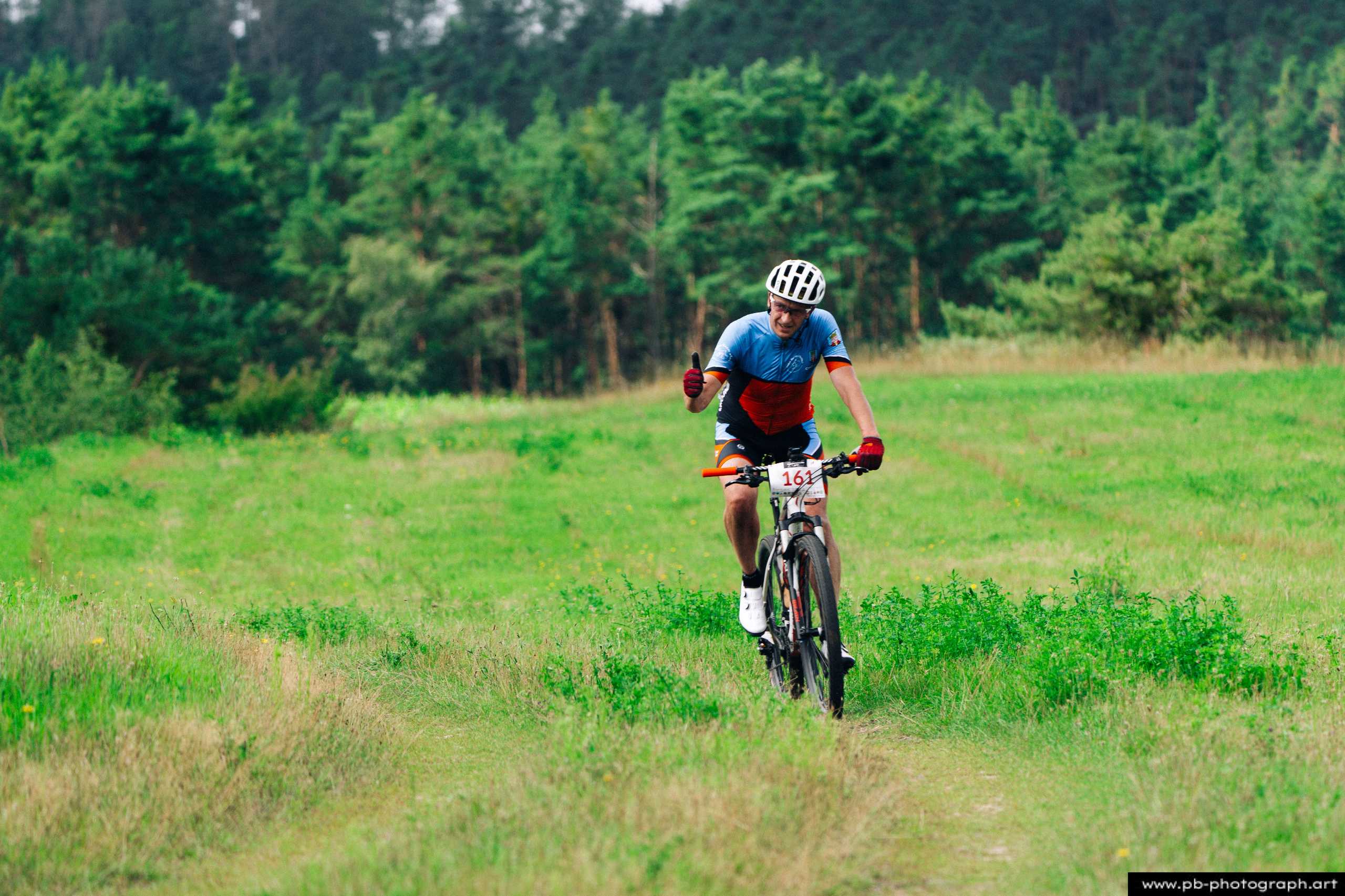 Ujęcie z drona zawodnika MTB na trasie wyścigu w Szczecinie, w otoczeniu zielonych pól i drzew.