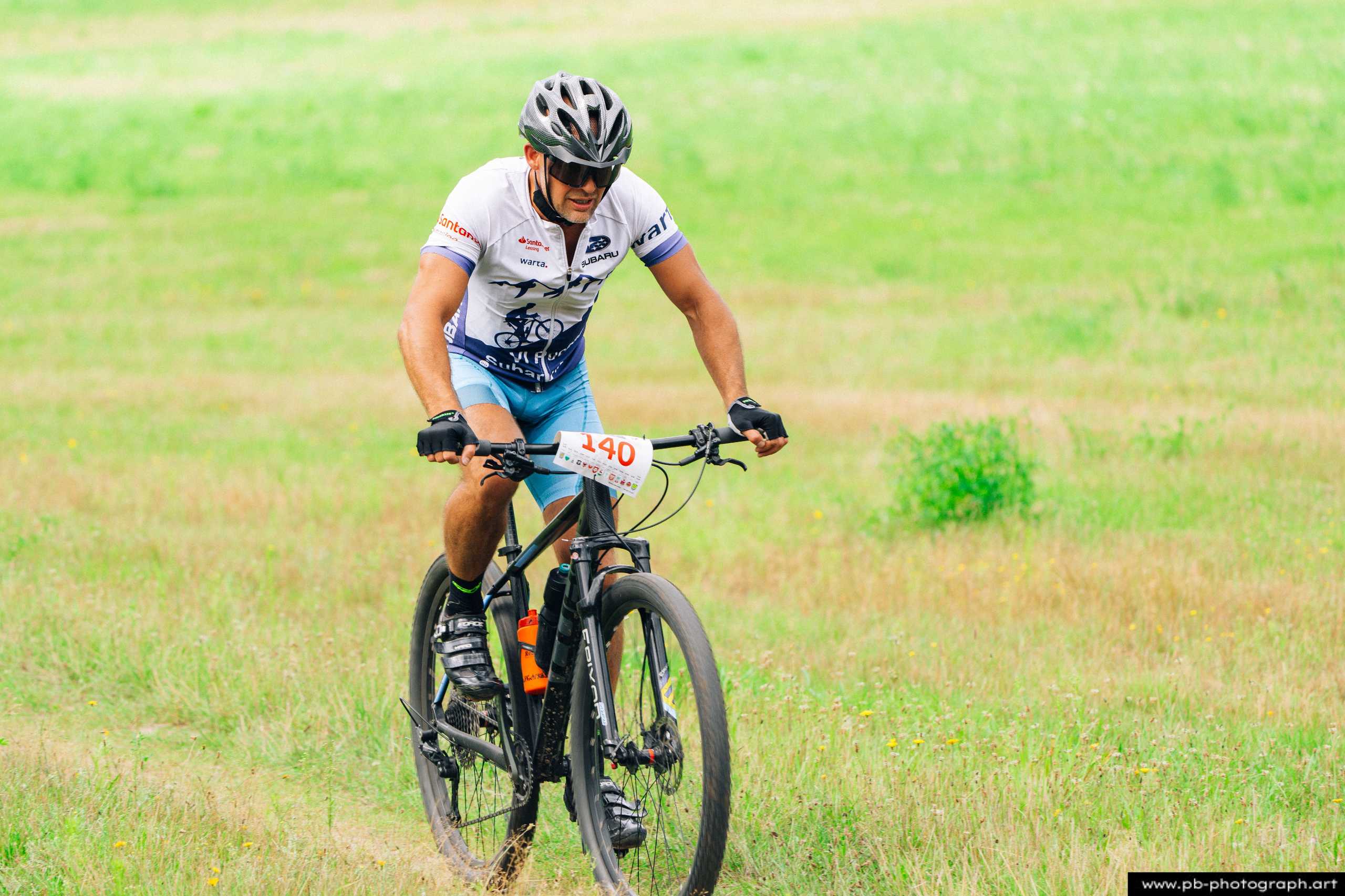 Zawodnik na rowerze górskim podczas wyścigu MTB w Szczecinie, pokonujący trawiasty teren.