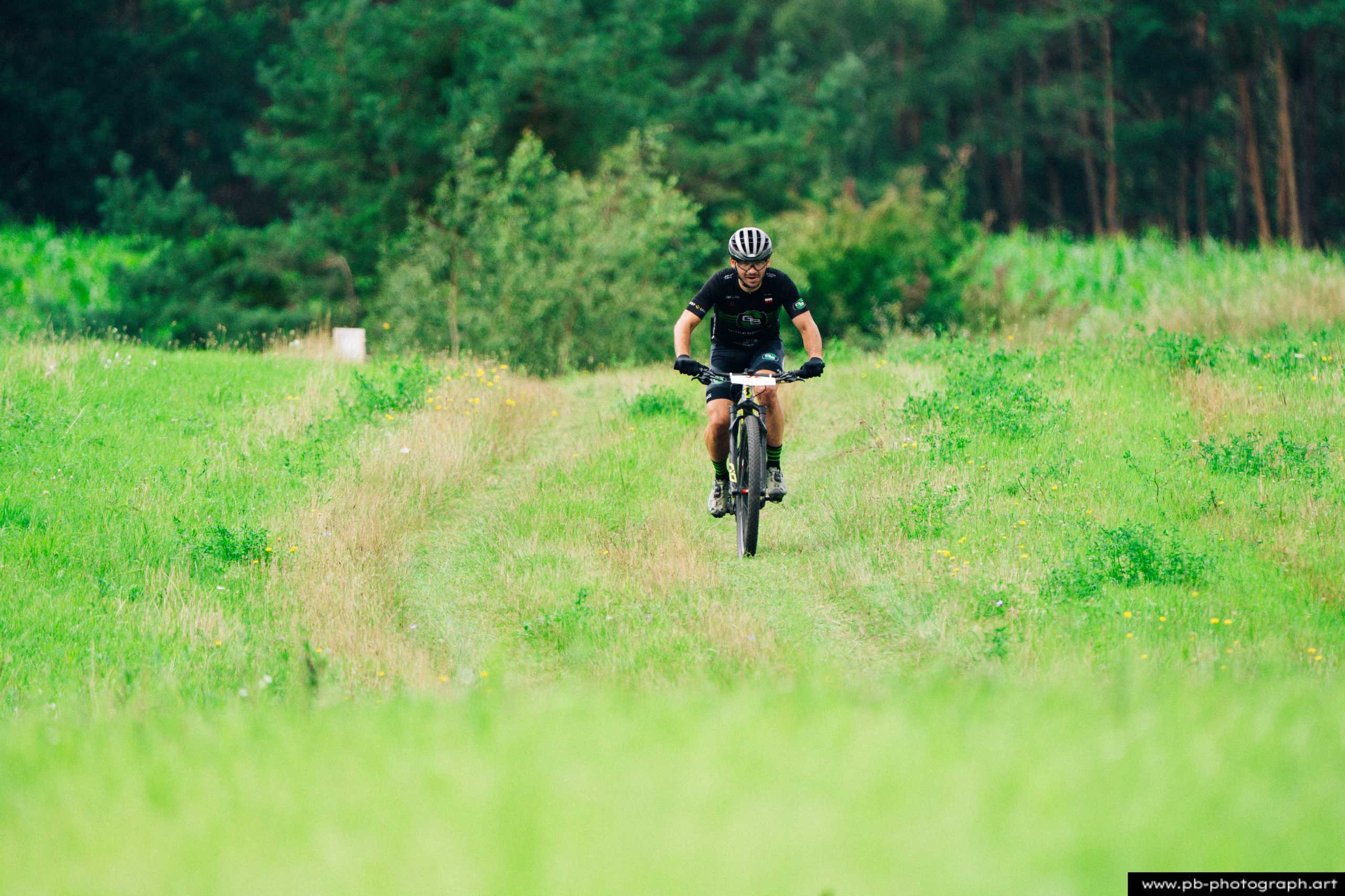 Ujęcie z drona zawodnika MTB na trasie wyścigu, otoczonego zielonymi łąkami w Szczecinie.