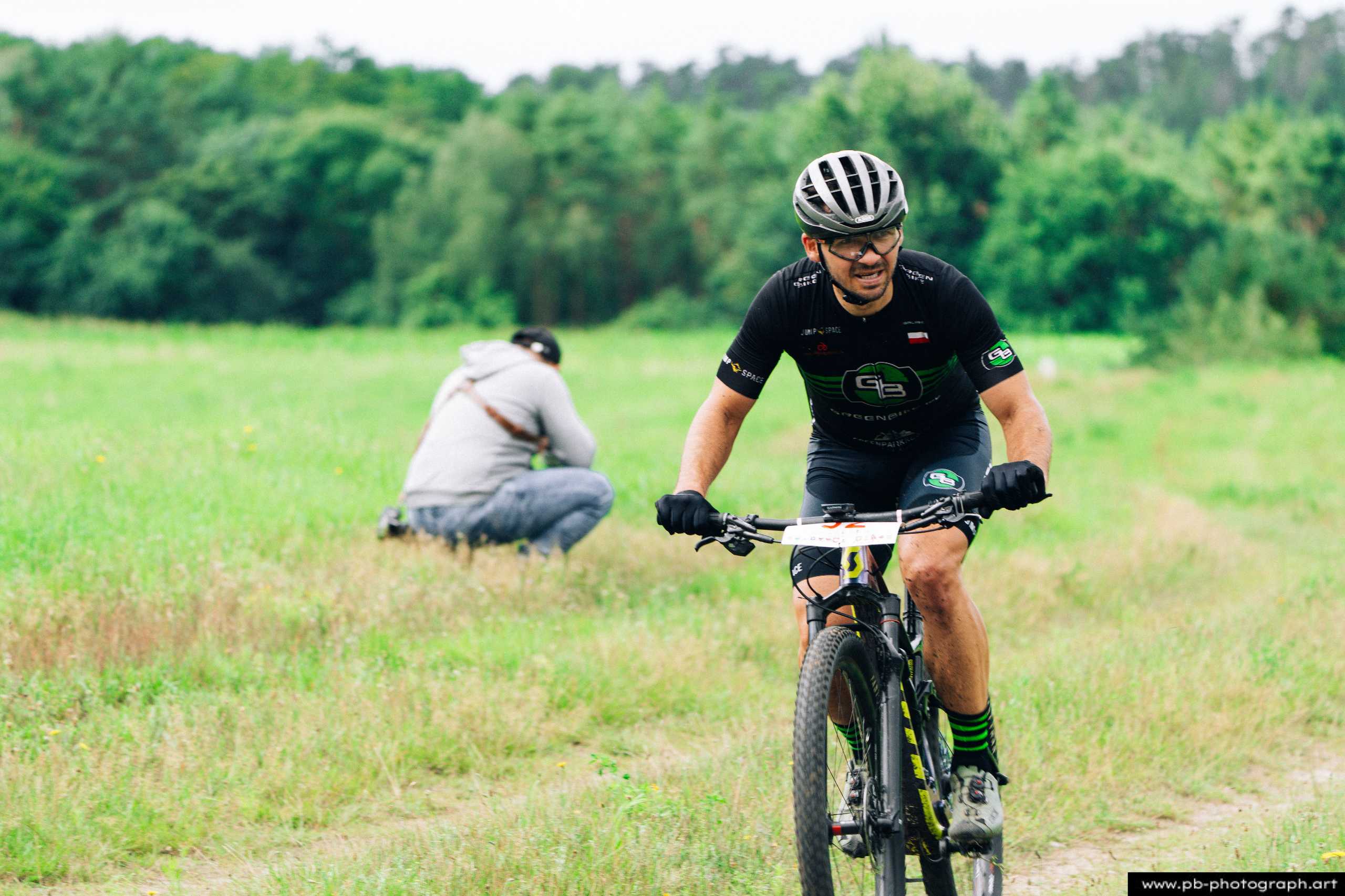Ujęcie z drona zawodnika MTB na trasie wyścigu w Szczecinie, z widokiem na zieleń otaczającą trasę.