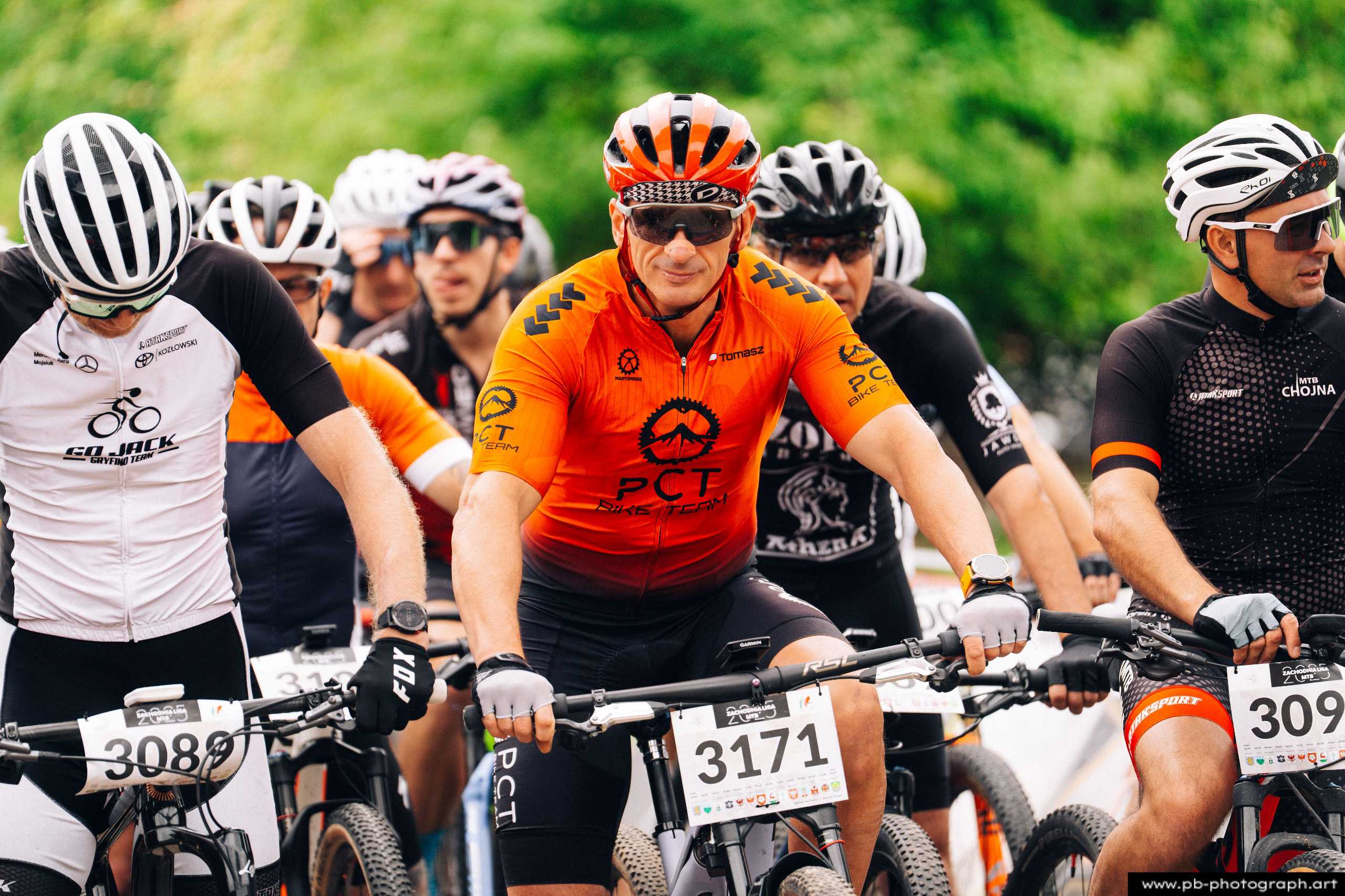 Fotografia z drona przedstawiająca zawodników MTB w pomarańczowych strojach na starcie wyścigu w Szczecinie.