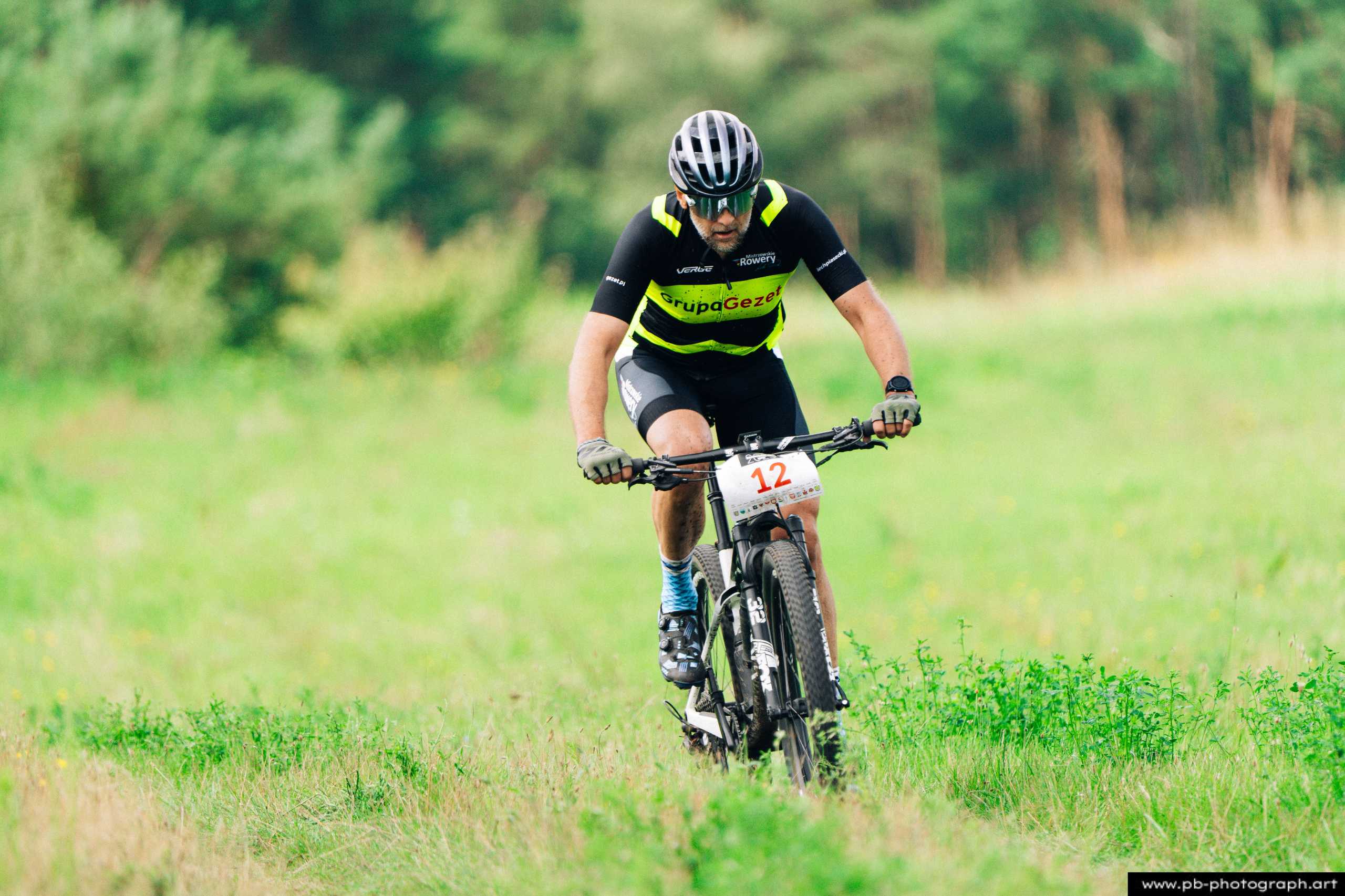 Ujęcie z drona zawodnika MTB na trasie wyścigu, pokonującego zieloną, leśną ścieżkę w Szczecinie.