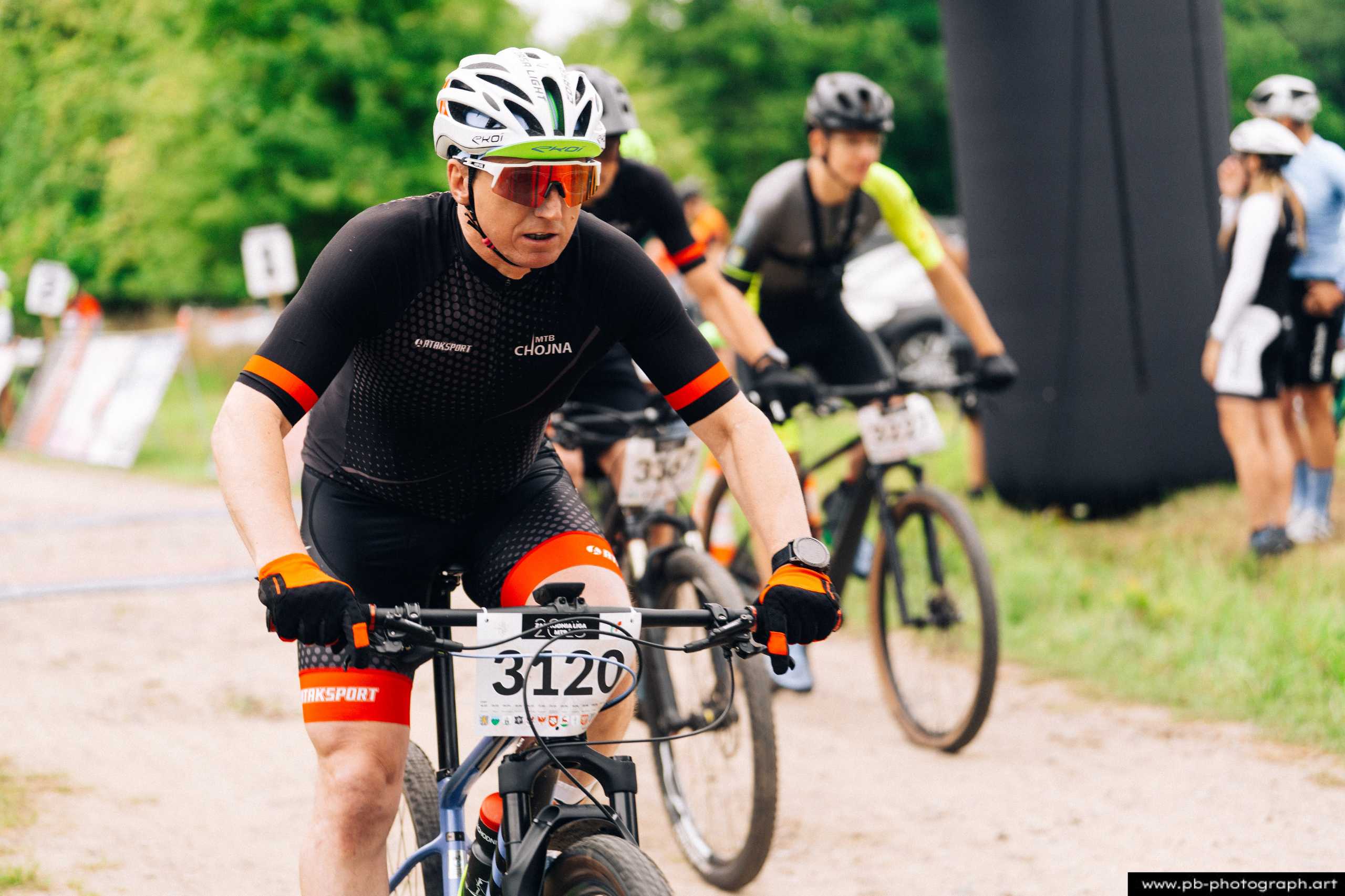 Zawodnik na rowerze górskim podczas wyścigu MTB w Szczecinie, zbliżenie na trasę i konkurentów w tle.