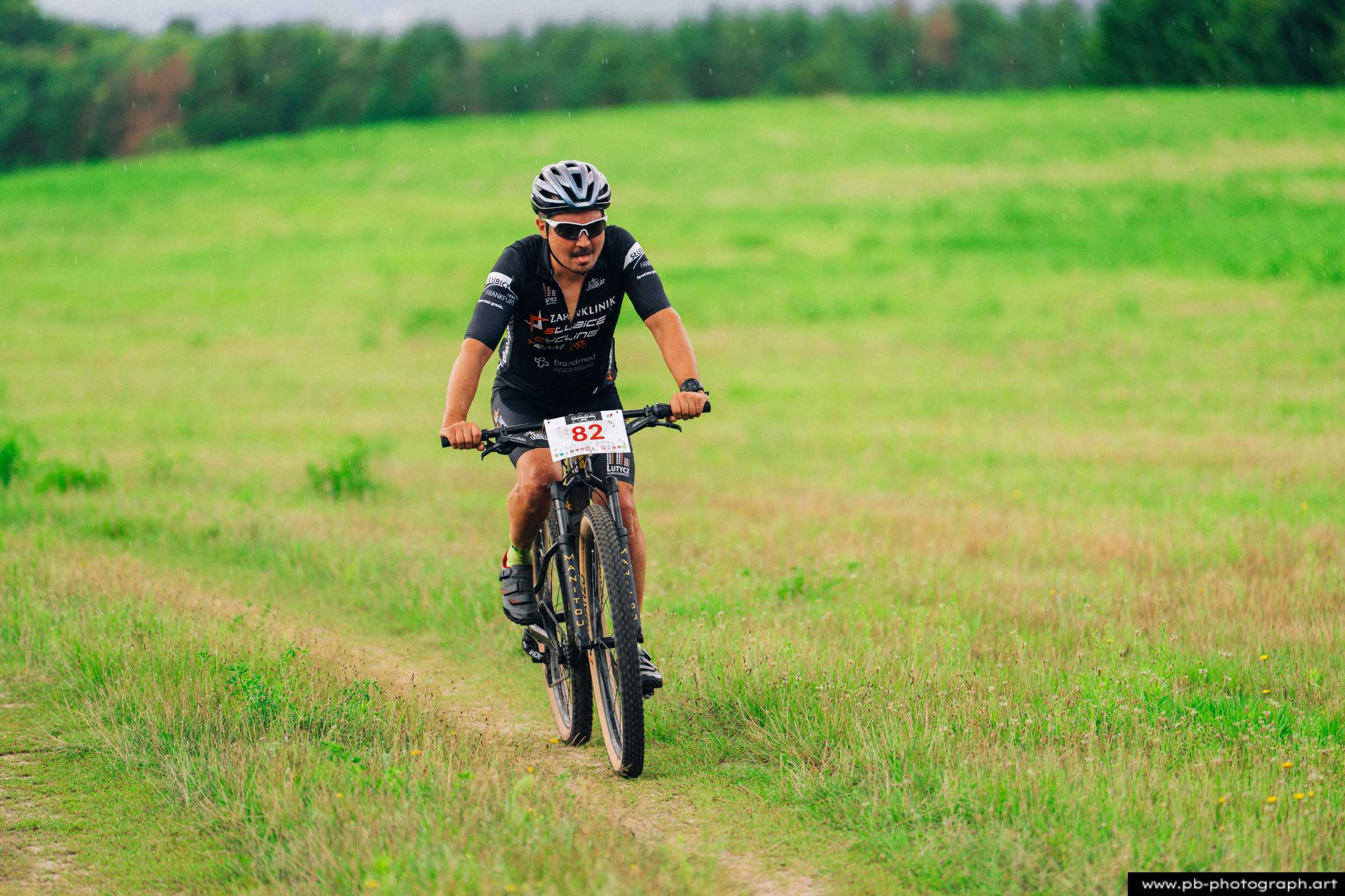 Zawodnik na rowerze górskim podczas wyścigu MTB w Szczecinie, na tle zielonego krajobrazu.