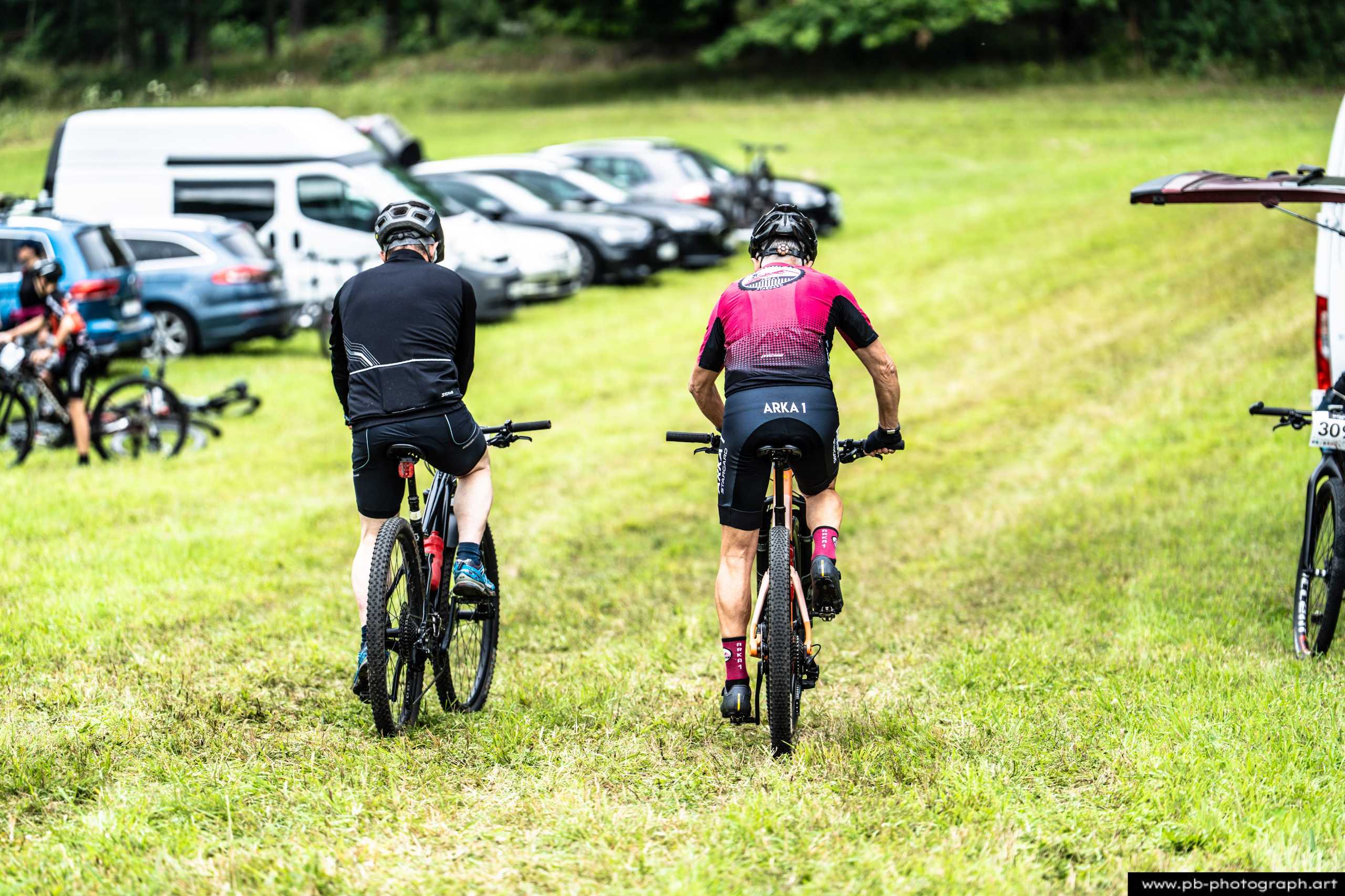 Zawodnicy MTB zmierzają w stronę trasy wyścigu, otoczeni przez zaparkowane samochody w Szczecinie.