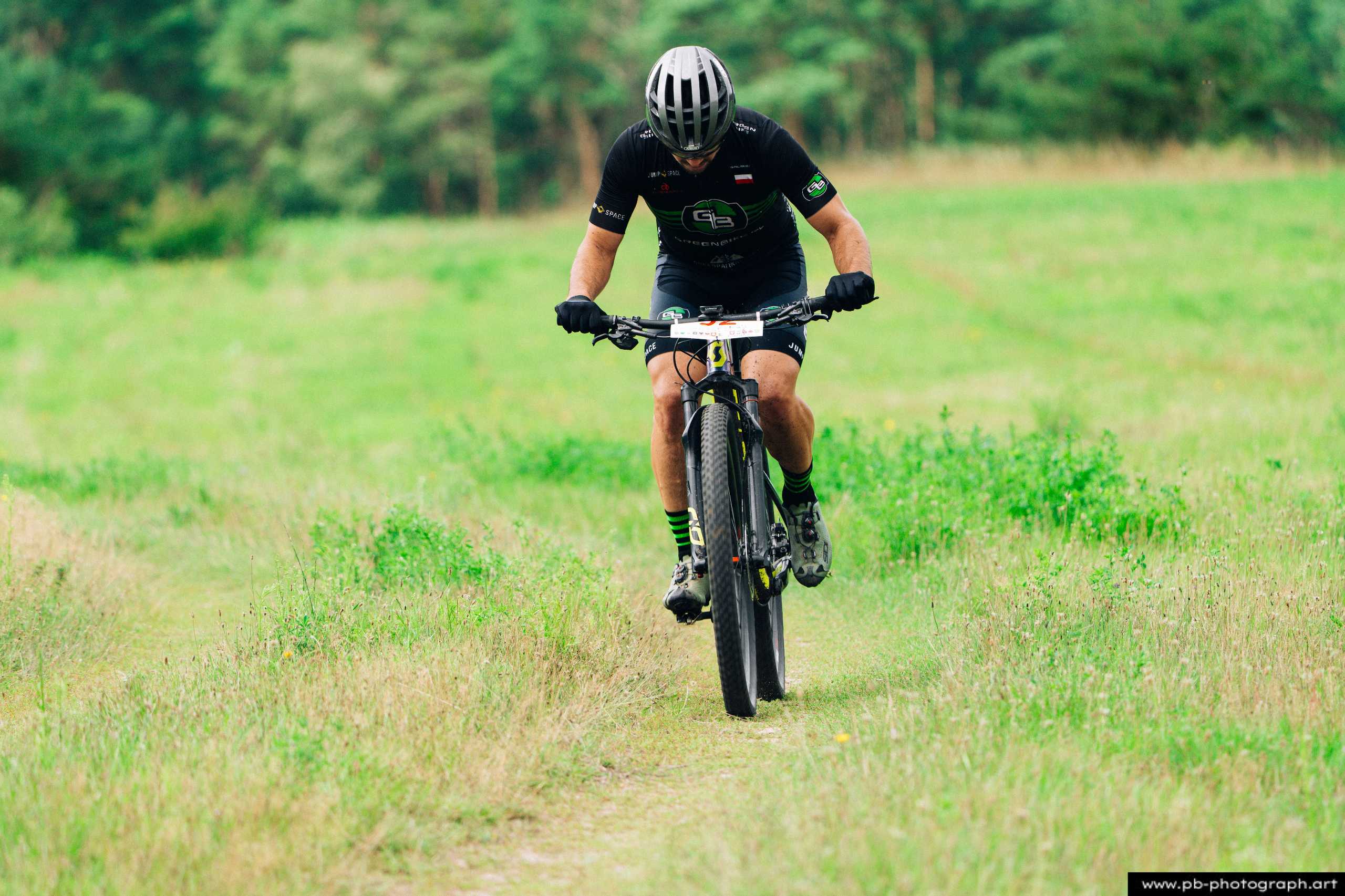 Zawodnik na rowerze górskim pokonujący trasę wyścigu MTB w Szczecinie, w otoczeniu zielonych pól.
