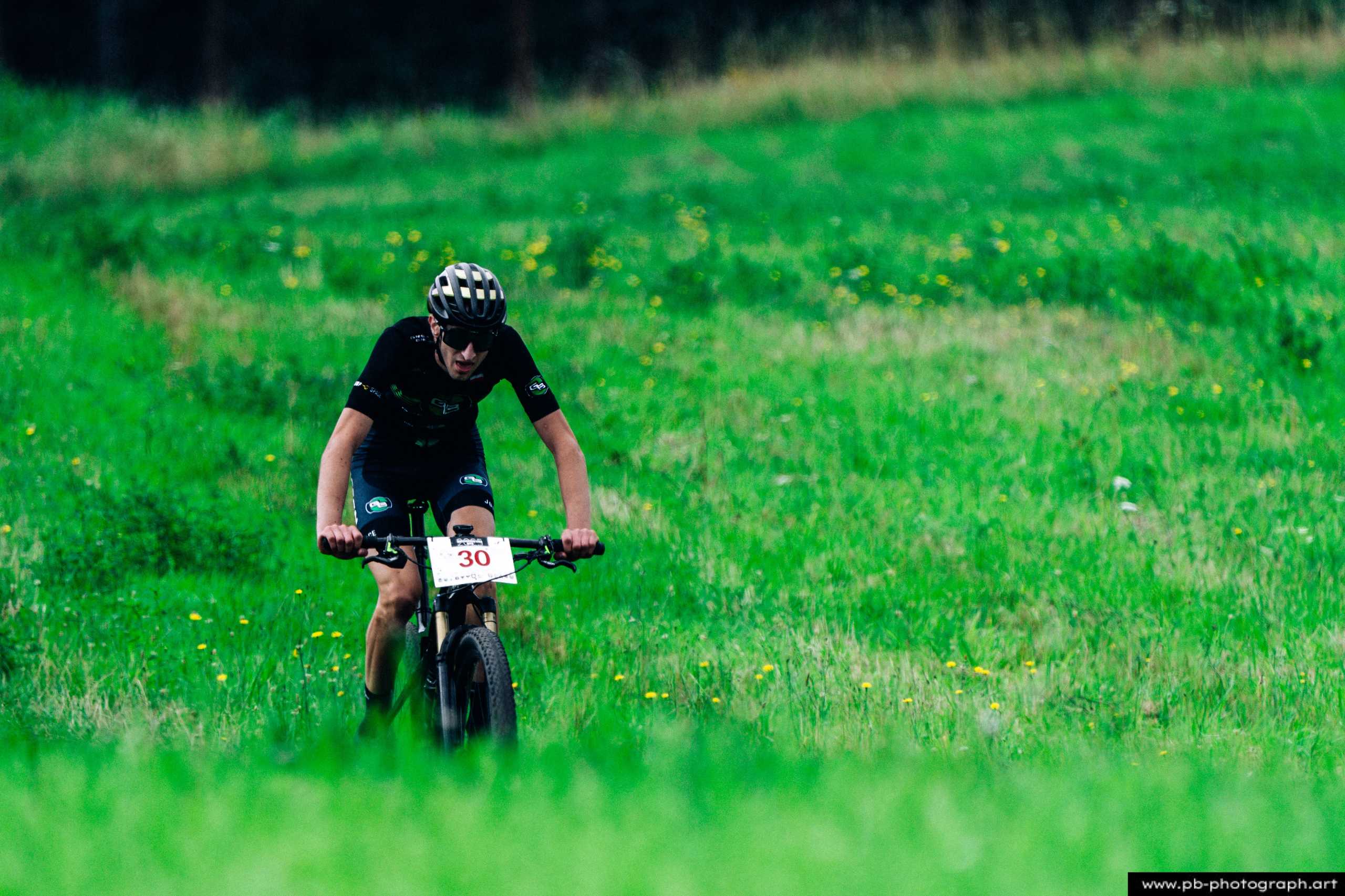 Zawodnik MTB na trasie wyścigu, pokonujący zieloną łąkę w Szczecinie podczas Rajdu MTD.