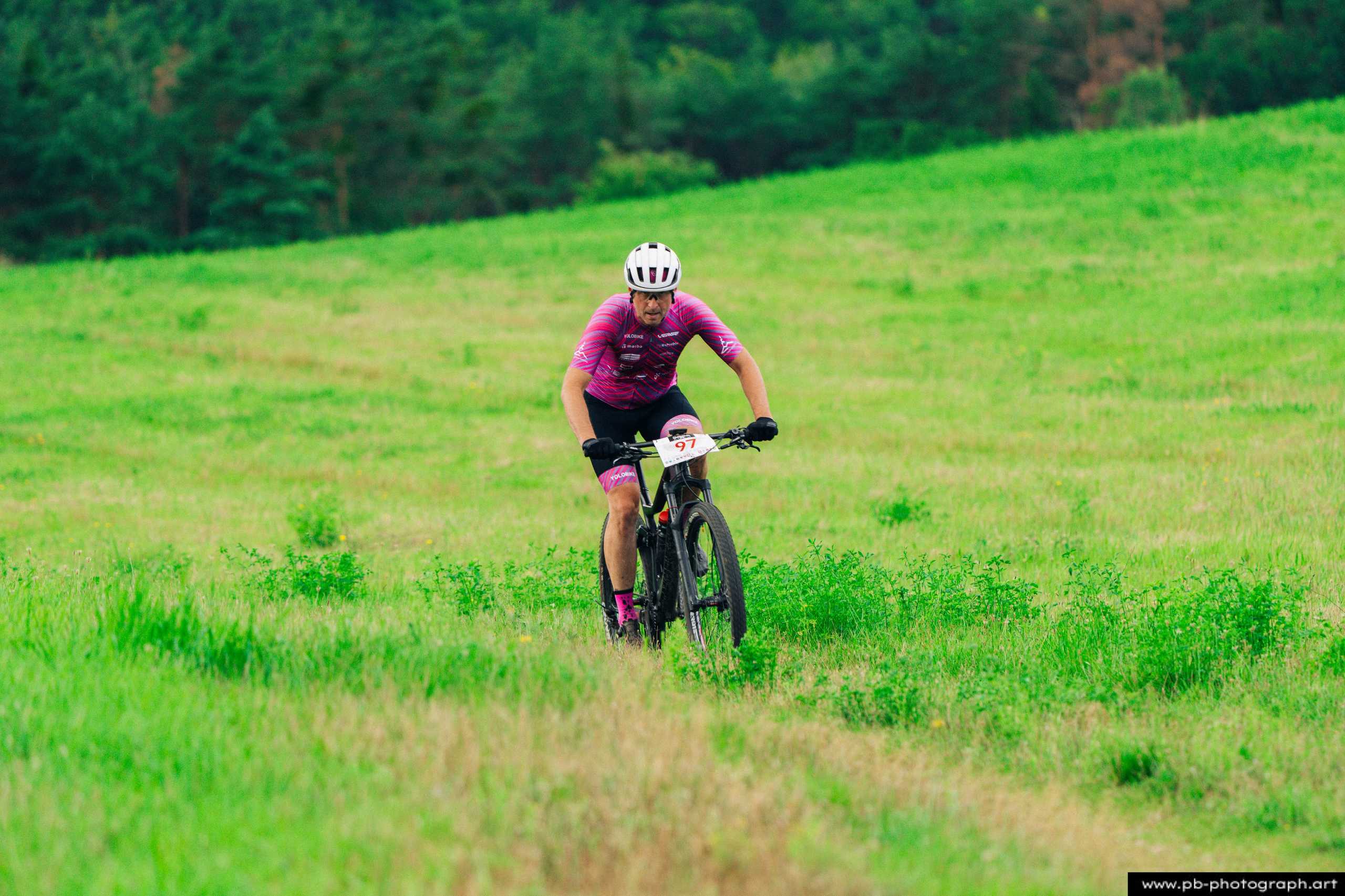 Zawodnik na rowerze górskim pokonujący zieloną trasę w lesie podczas wyścigów MTB w Szczecinie.