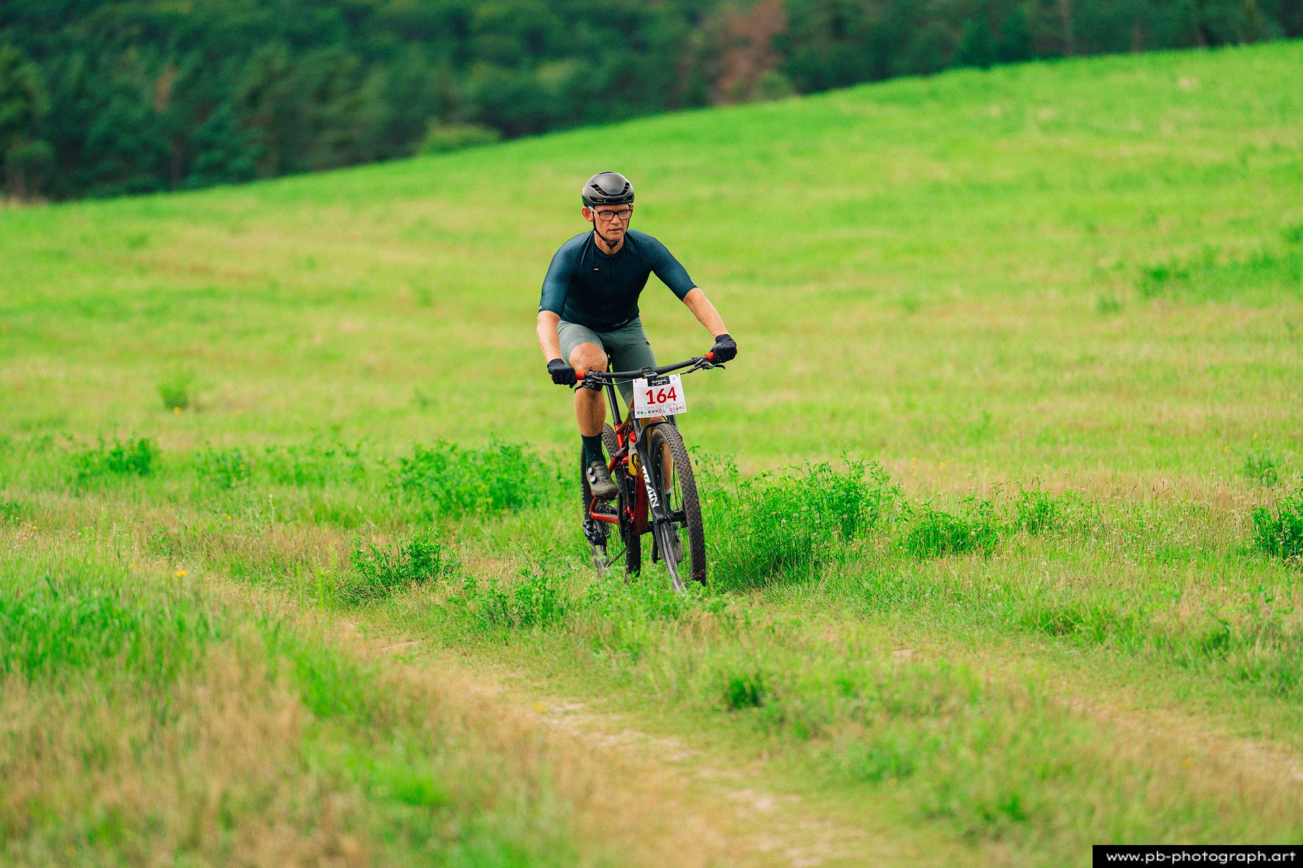 Zawodnik na rowerze górskim podczas wyścigu MTB w Szczecinie, pokonujący zieloną trasę w terenie.