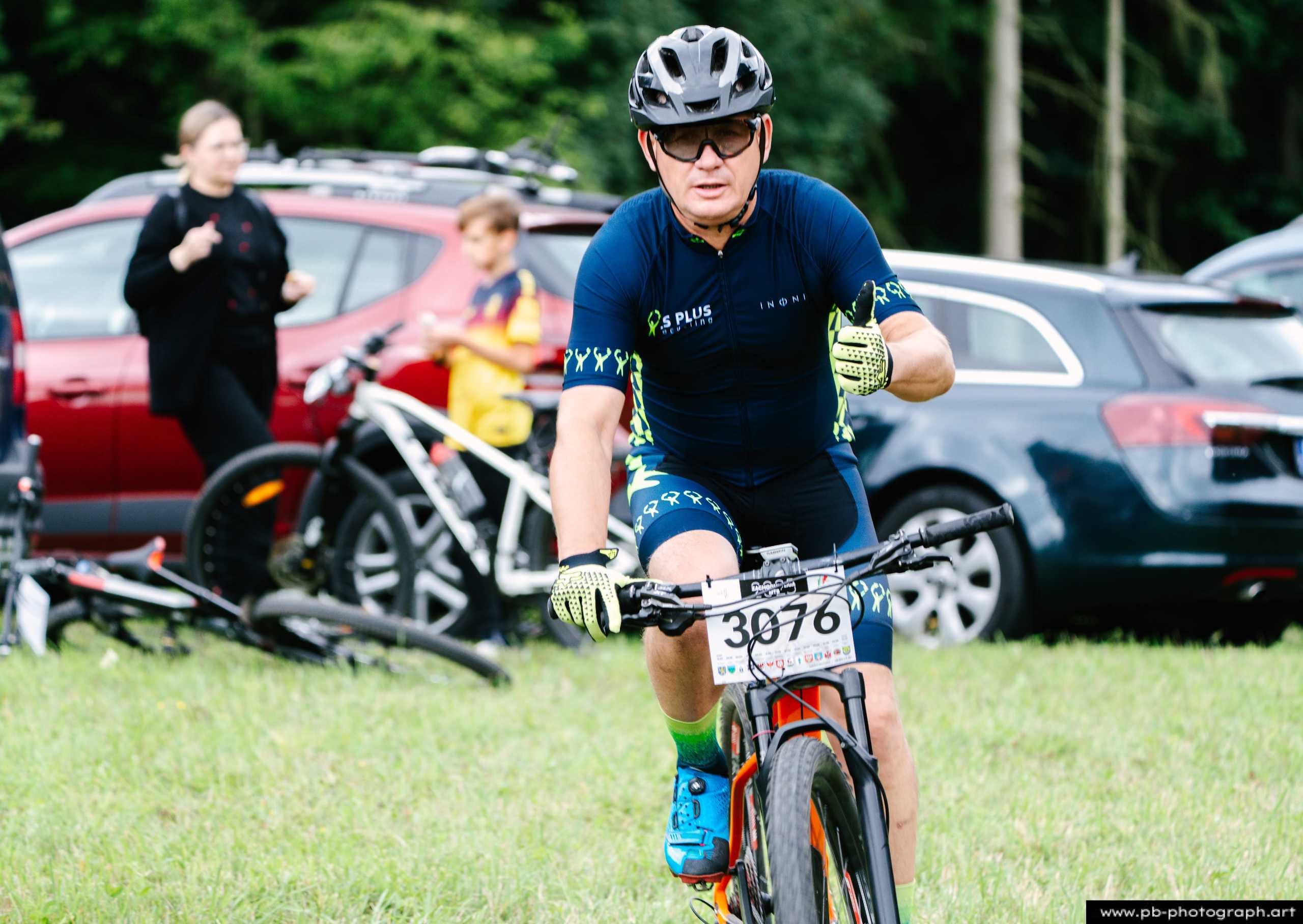 Zawodnik na rowerze górskim podczas wyścigu MTB w Szczecinie, z tłem samochodów i innych uczestników.