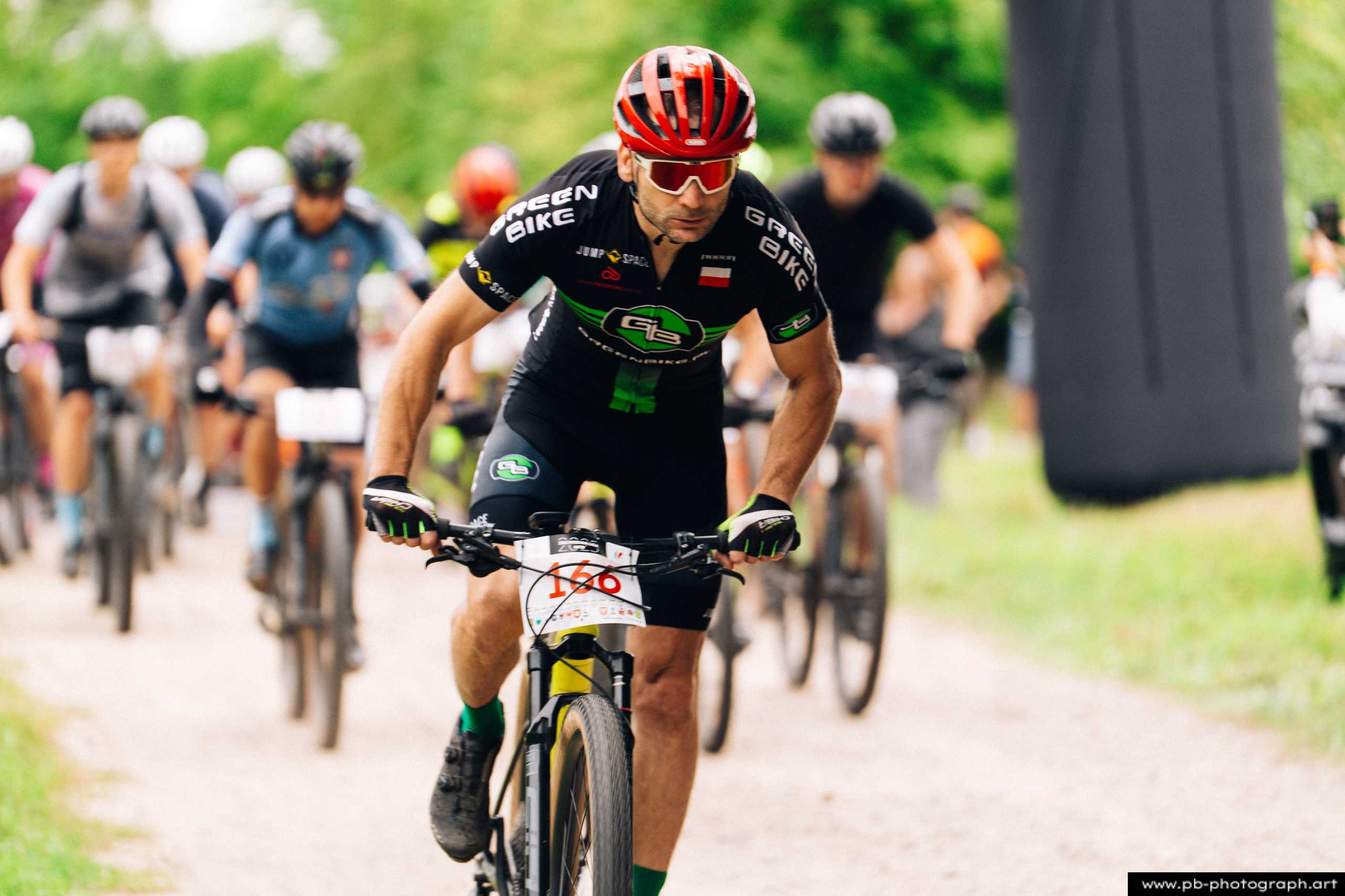 Fotografia z drona podczas wyścigów MTB w Szczecinie — zawodnik w akcji na trasie, w tle grupa uczestników.