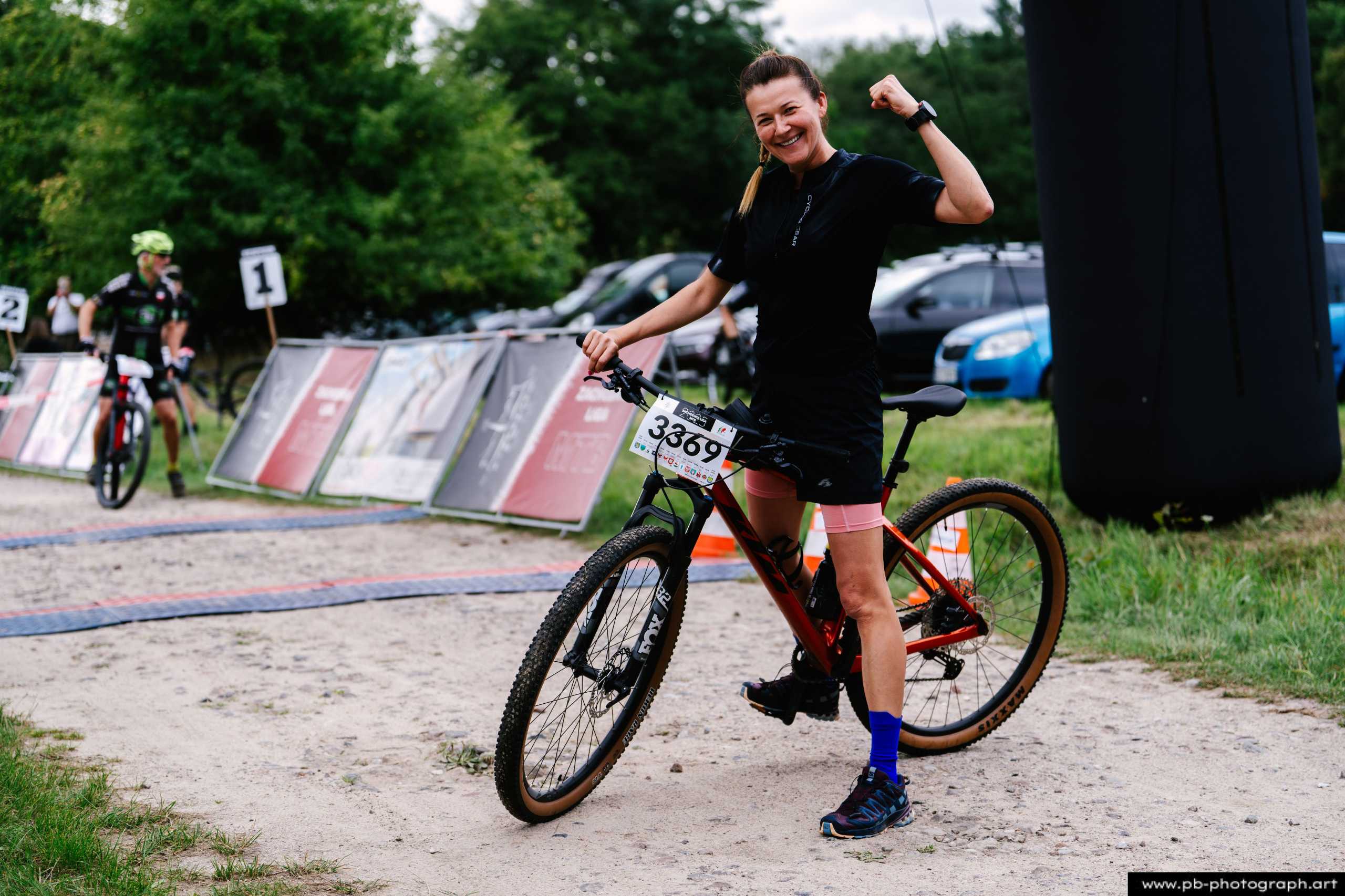 Zawodniczka MTB w radosnej pozie przy rowerze na trasie wyścigu w Szczecinie.