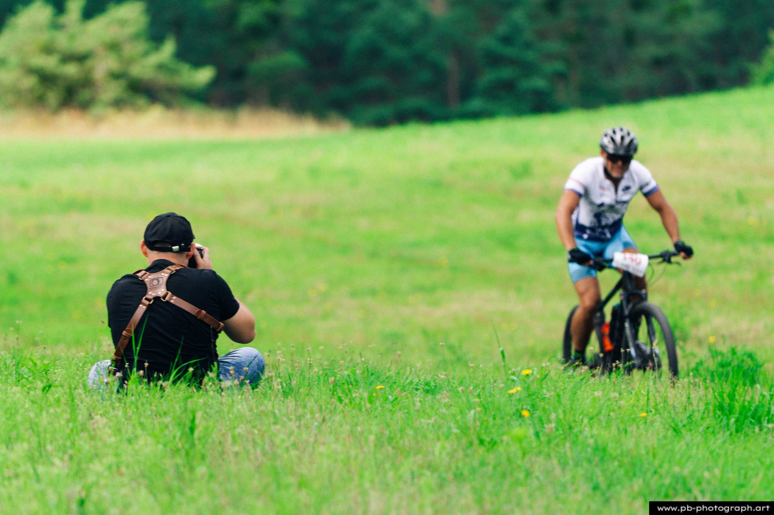 Ujęcie z drona pokazujące kolarza MTB w akcji na zielonym tle, z fotografem w tle na trawie w Szczecinie.