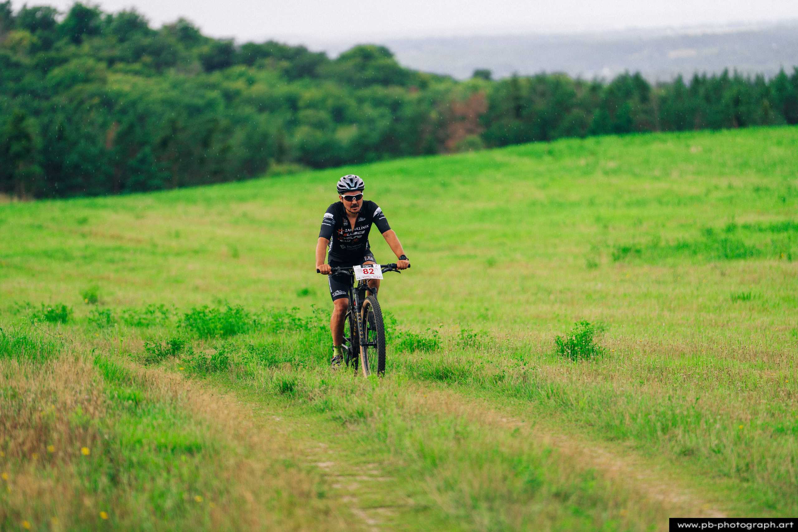 Ujęcie z drona zawodnika MTB na zielonej trasie wyścigu w Szczecinie, otoczonego malowniczym krajobrazem.