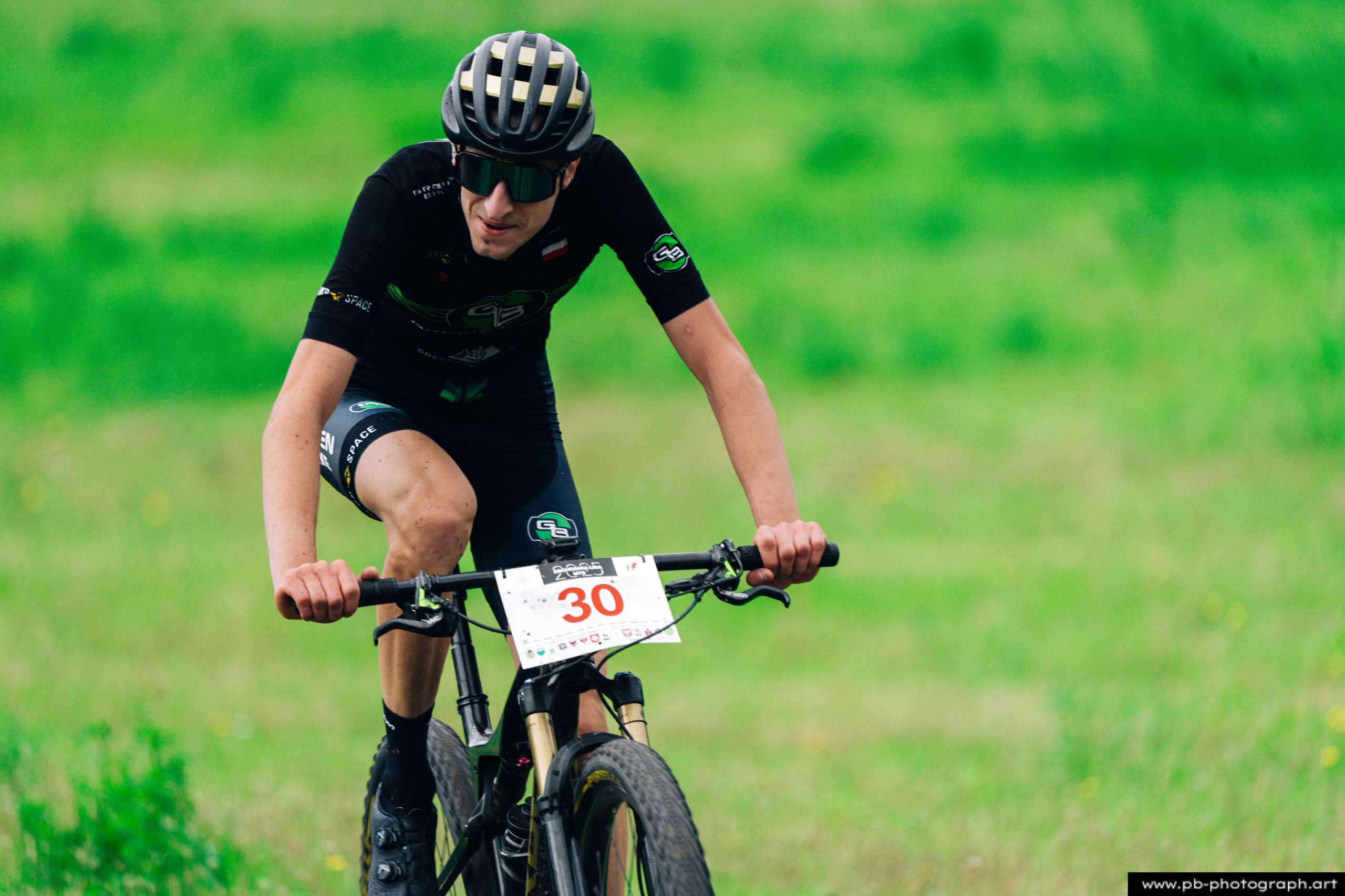 Fotografia z drona podczas wyścigu MTB w Szczecinie — zawodnik na rowerze w dynamicznej akcji na zielonym tle.