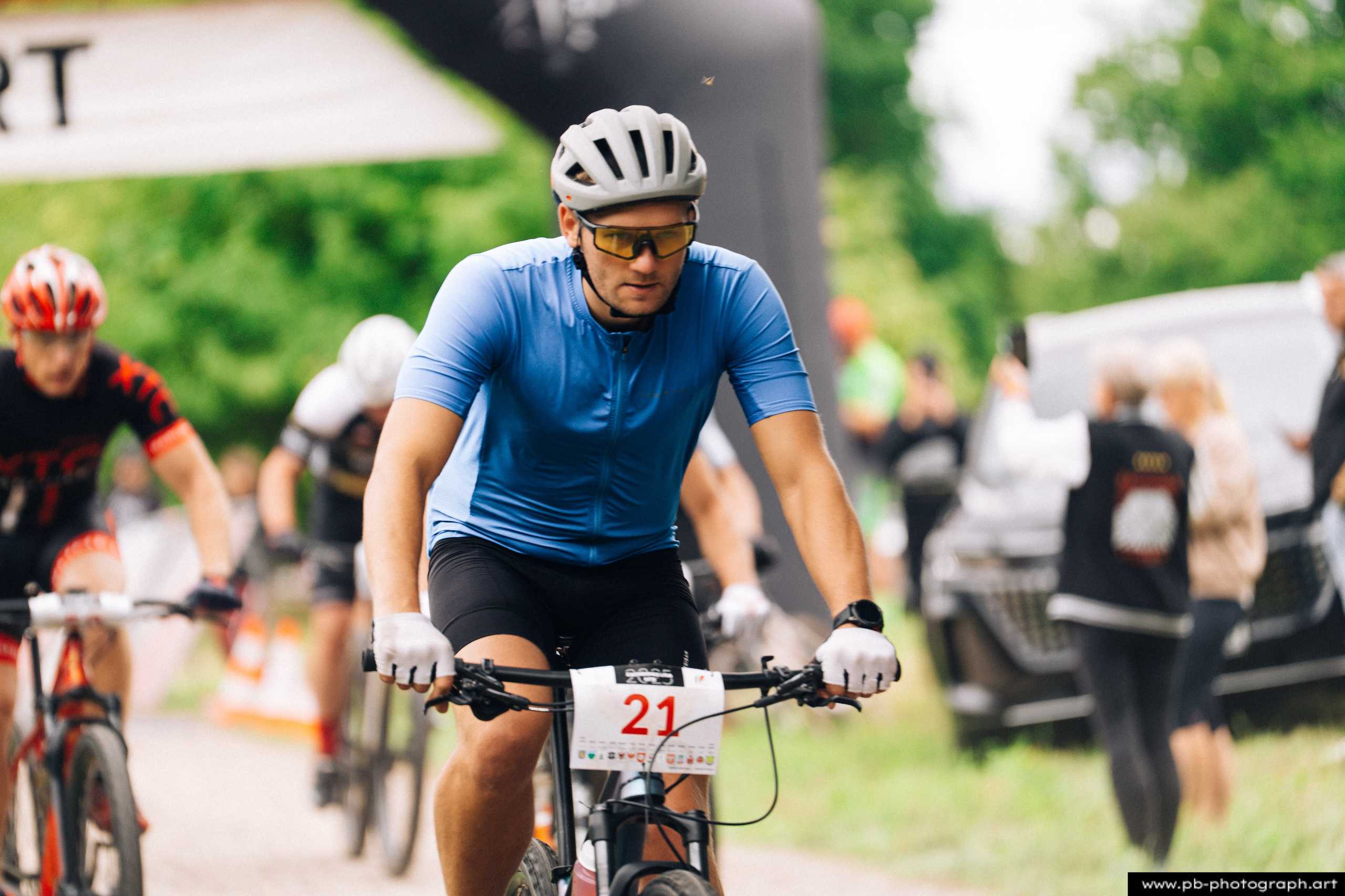 Ujęcie z drona zawodnika MTB na trasie wyścigu w Szczecinie, z numerem startowym 21, w niebieskiej koszulce.