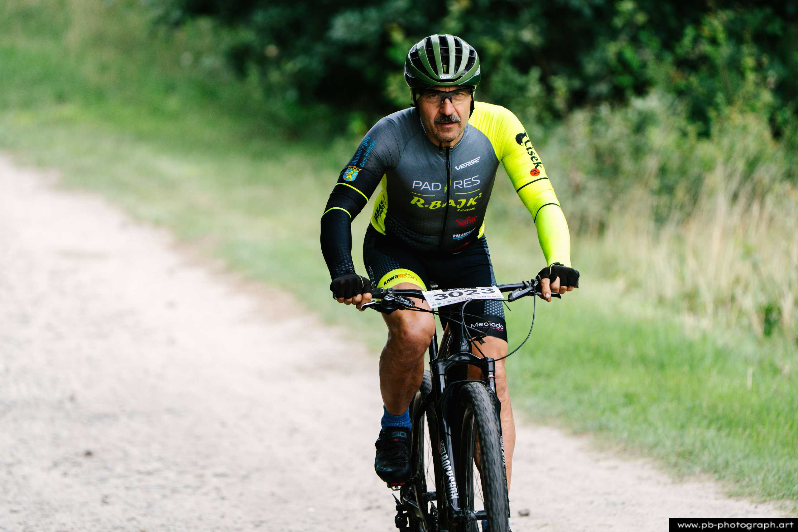 Ujęcie z drona zawodnika MTB na trasie wyścigu w Szczecinie, w tle zieleń i droga gruntowa.