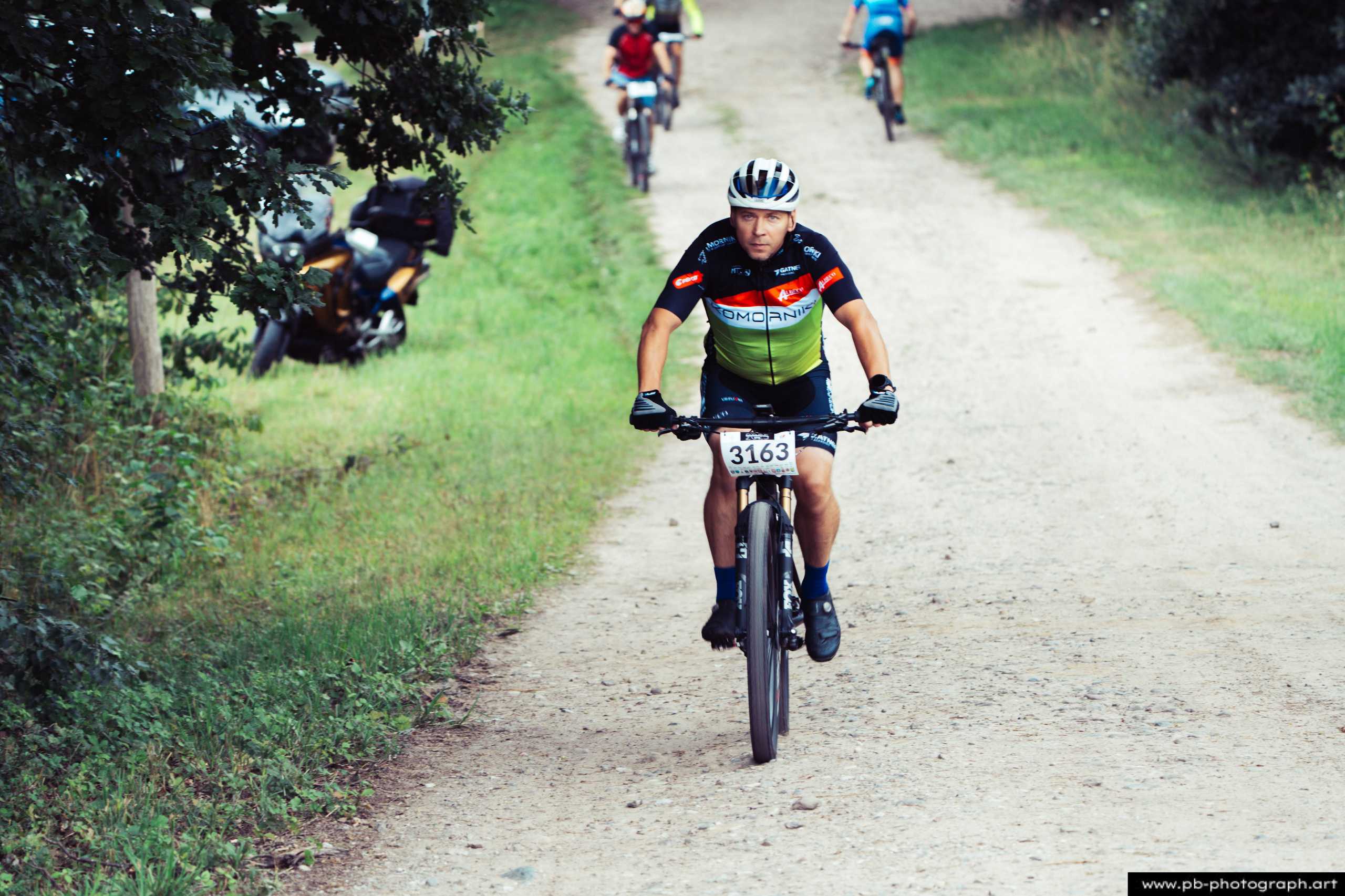 Zawodnik na rowerze górskim podczas wyścigu MTB w Szczecinie, zbliżenie na trasę i zieleń w tle.