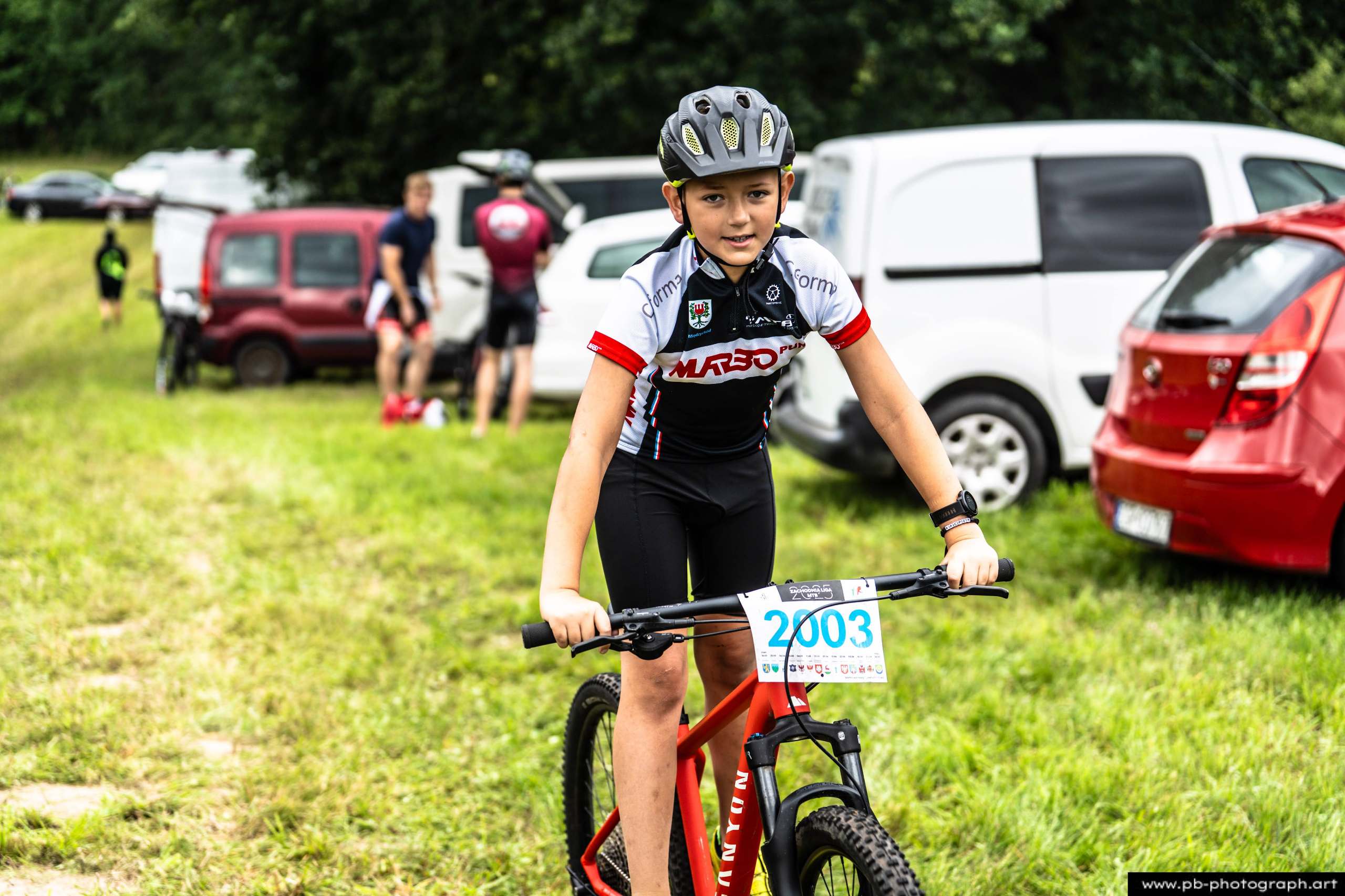Młody zawodnik na rowerze górskim przed startem wyścigu MTB w Szczecinie, z samochodami w tle.