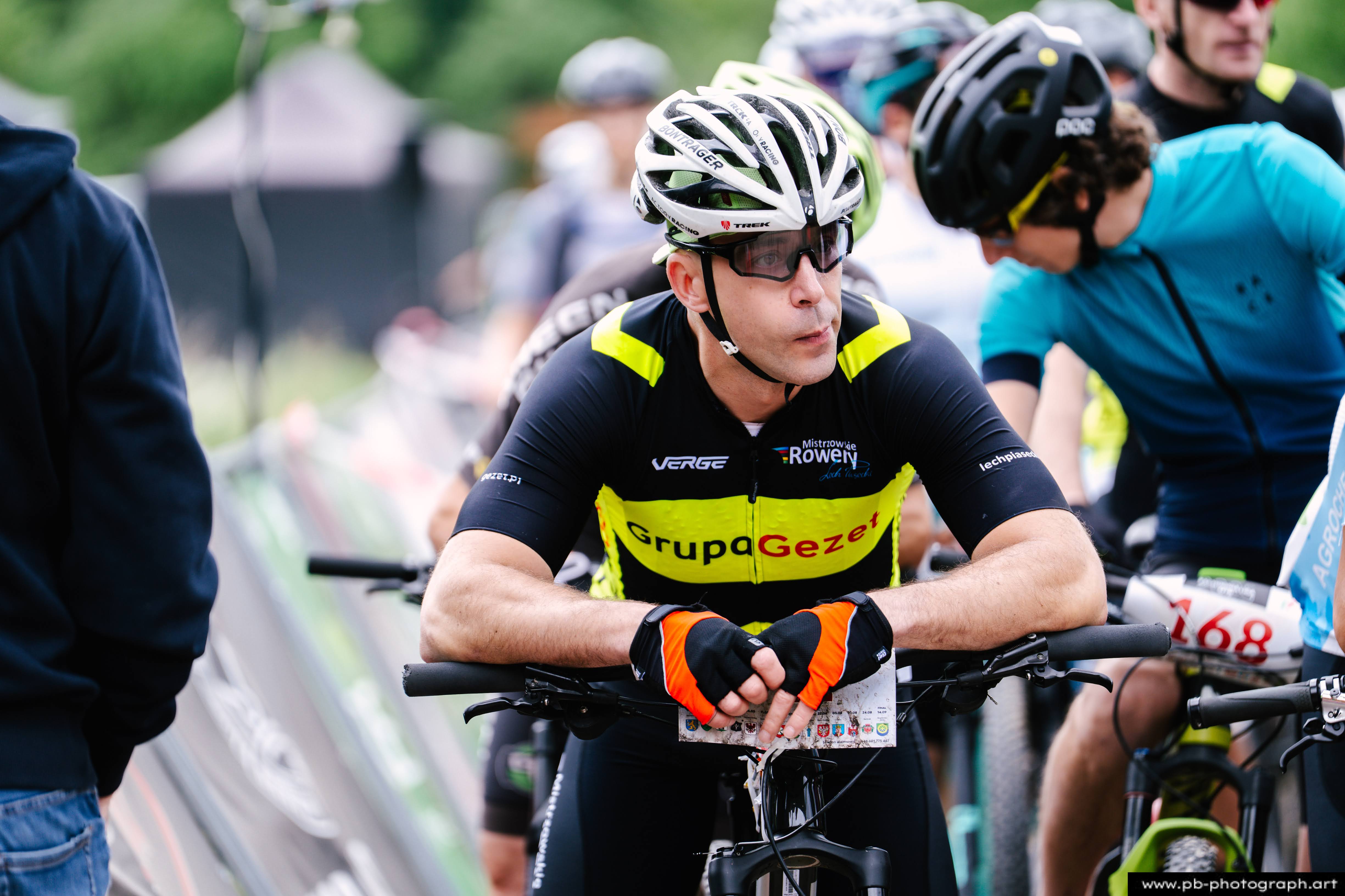 Zawodnik w kasku i rękawiczkach czeka na start wyścigu MTB w Szczecinie, z rowerem obok siebie.