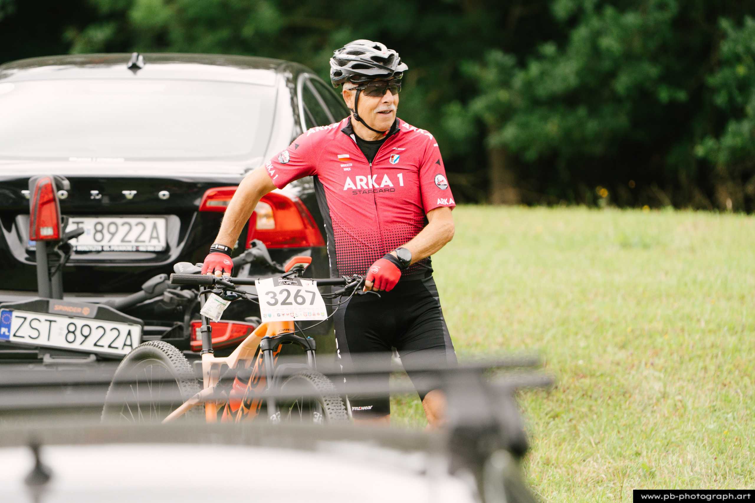 Zawodnik w czerwonym stroju przygotowuje się do wyścigu MTB obok swojego roweru i samochodu w Szczecinie.